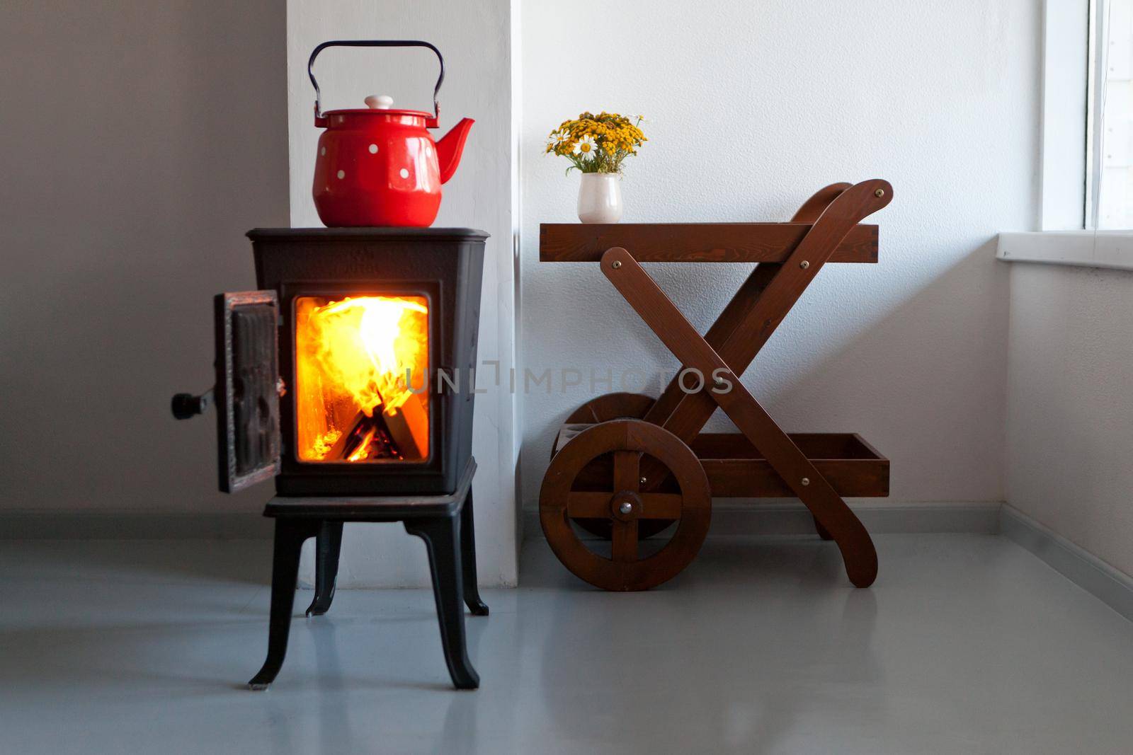 red kettle boiling on a retro stove in the kitchen. open fireplace. Focus on a spout. country home design with furnace at the interior