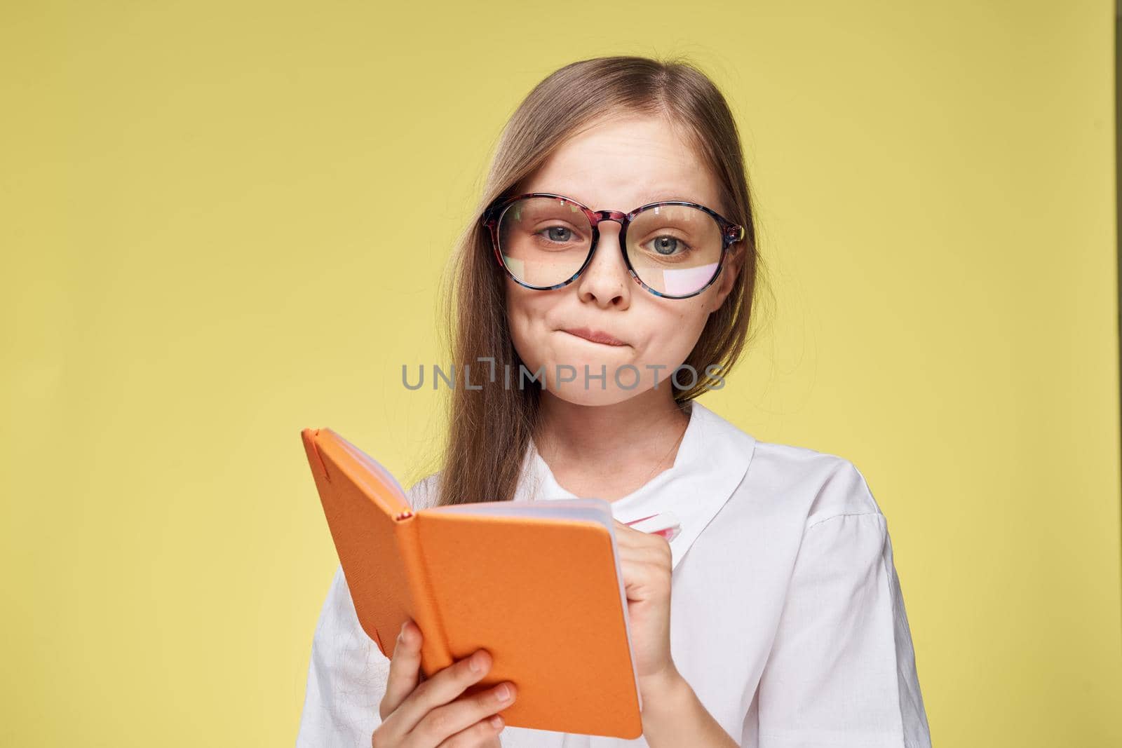 schoolgirl with textbook in hands learning childhood yellow background. High quality photo