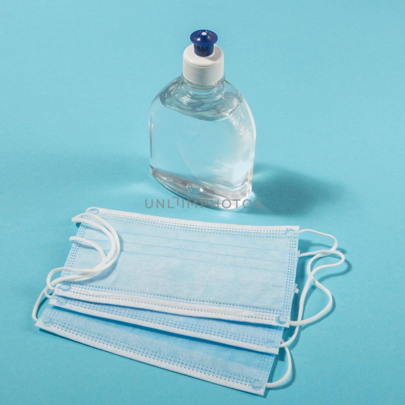 Alcohol gel hand sanitizer and disposable hygienic mask on blue background