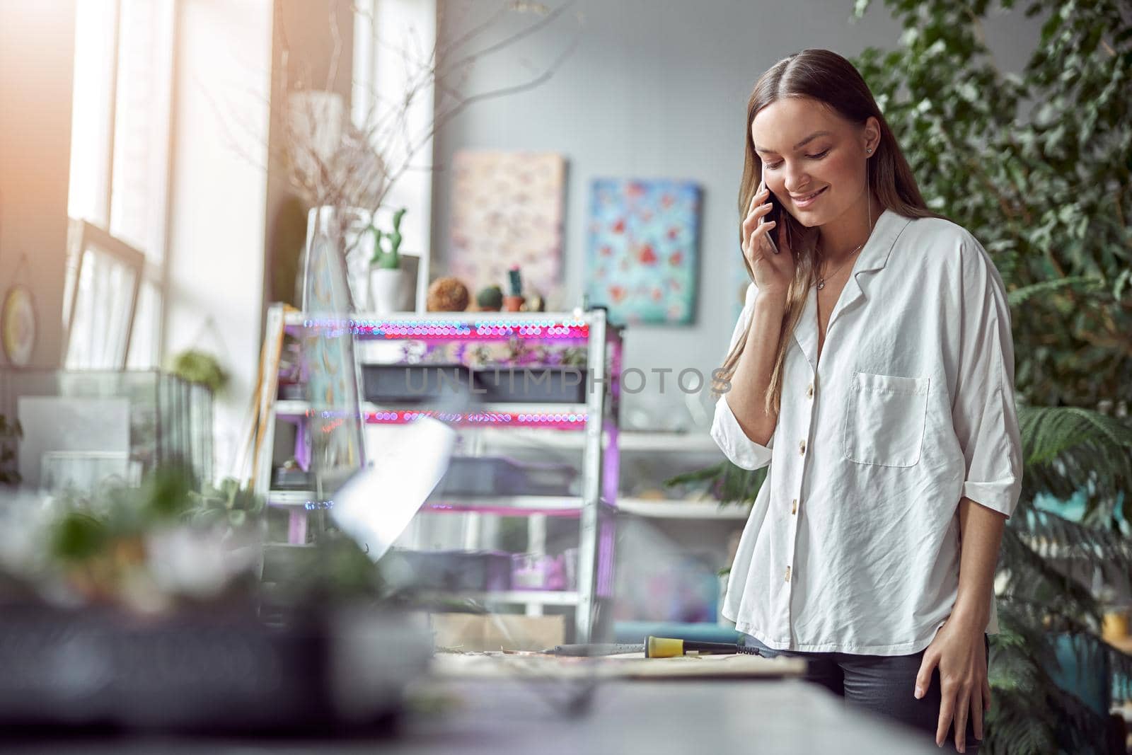 Confident female florist is working with dryed flowers in cozy flower shop while speaking on the smartphone