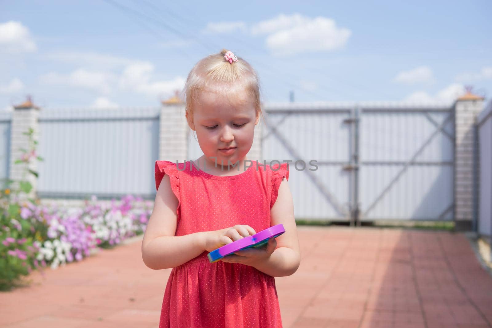 Cute caucasian fair hair girl in pink dress is playing and showing funny trendy silicone antistress colorful toy popit. Push Popper fidget toy is the ideal toy to get rid of your frustration or stress. Kids being kids LGBTQ colors Vertical