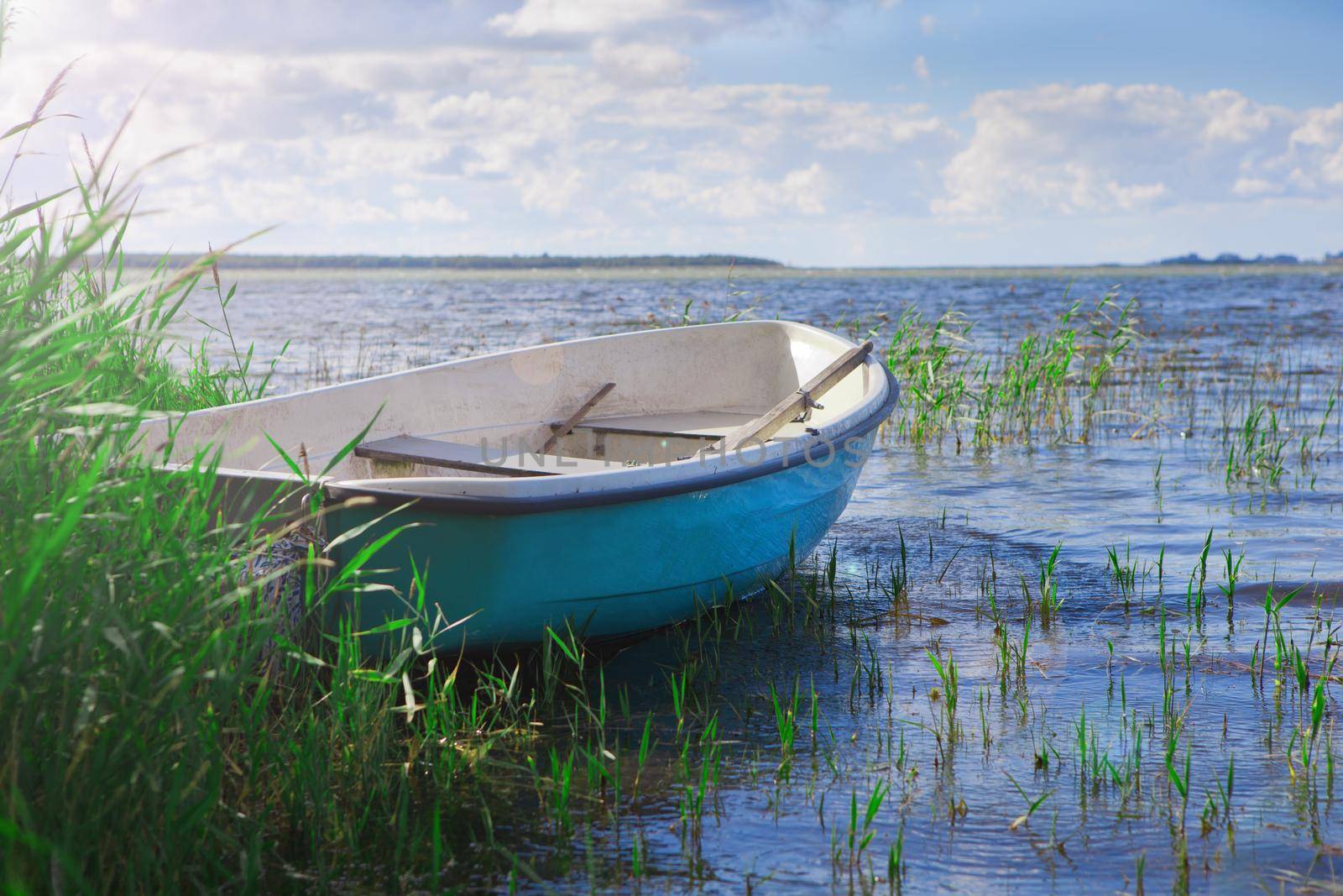 Old fishing boat. blue fishing boat on the sea near the grass or seaweed at summer time. Sunny weather and flare light.