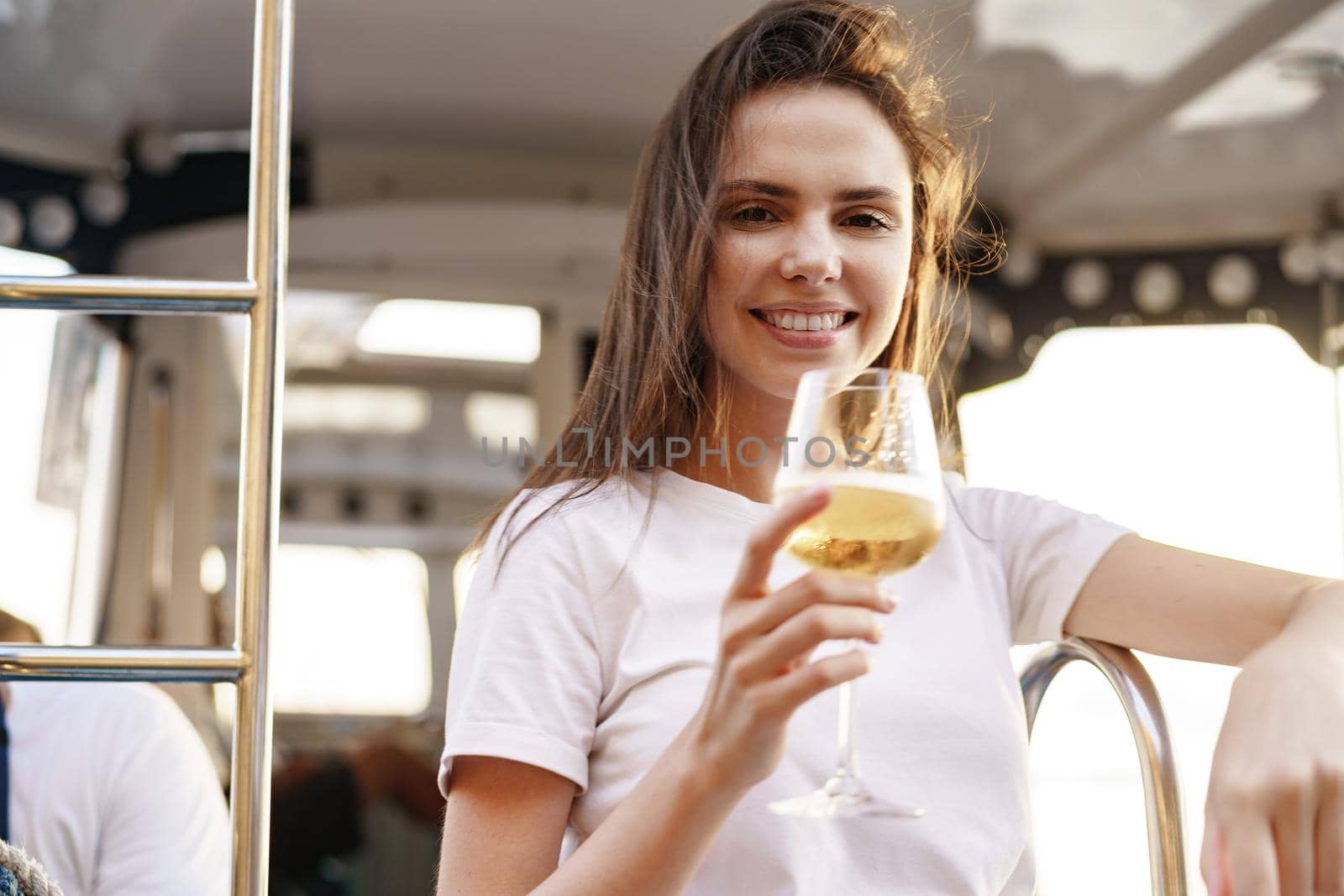 Young woman holding a wineglass and sitting on deck of sailing yacht boat