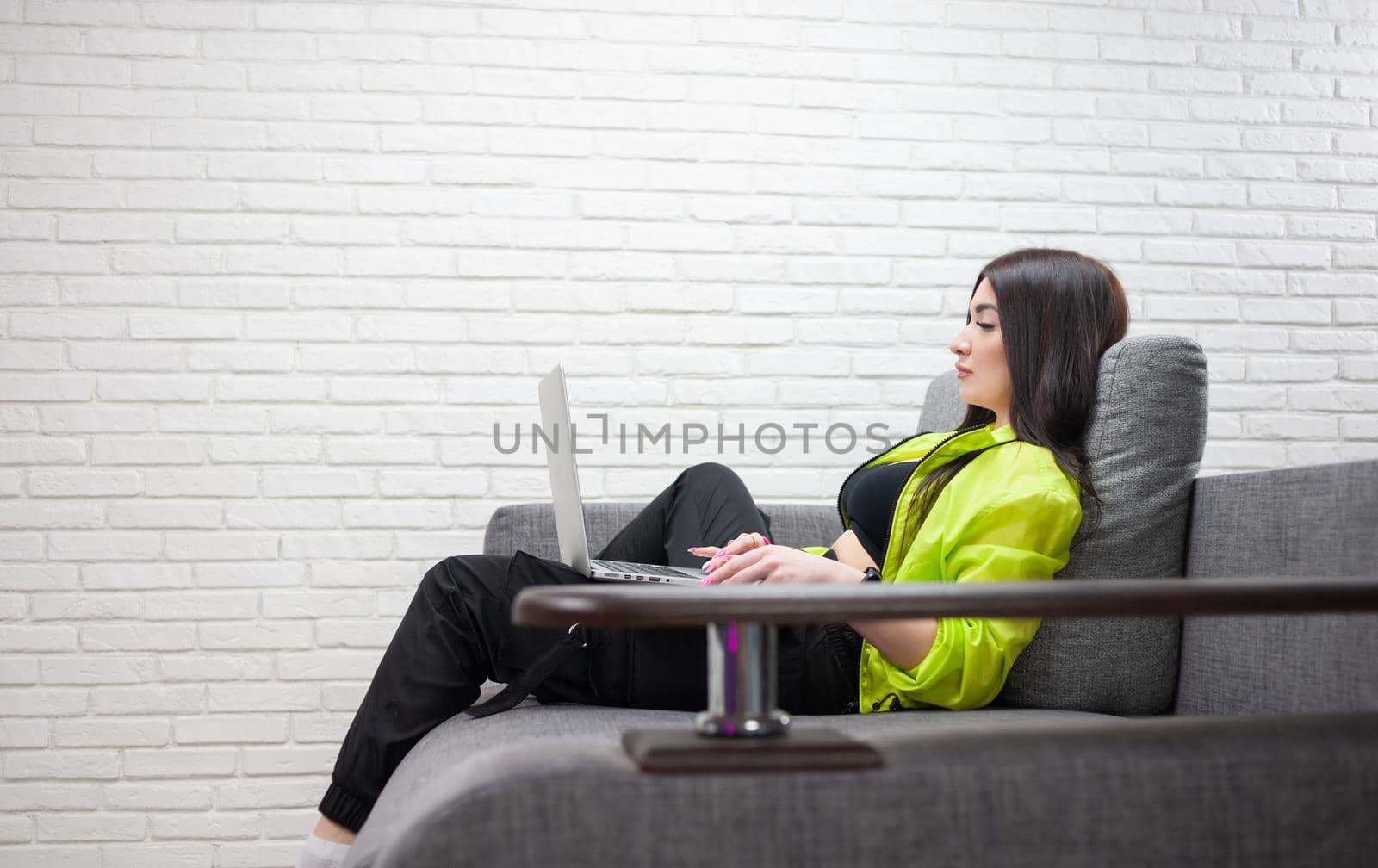 a girl in a bright tracksuit with a laptop on the couch by Rotozey