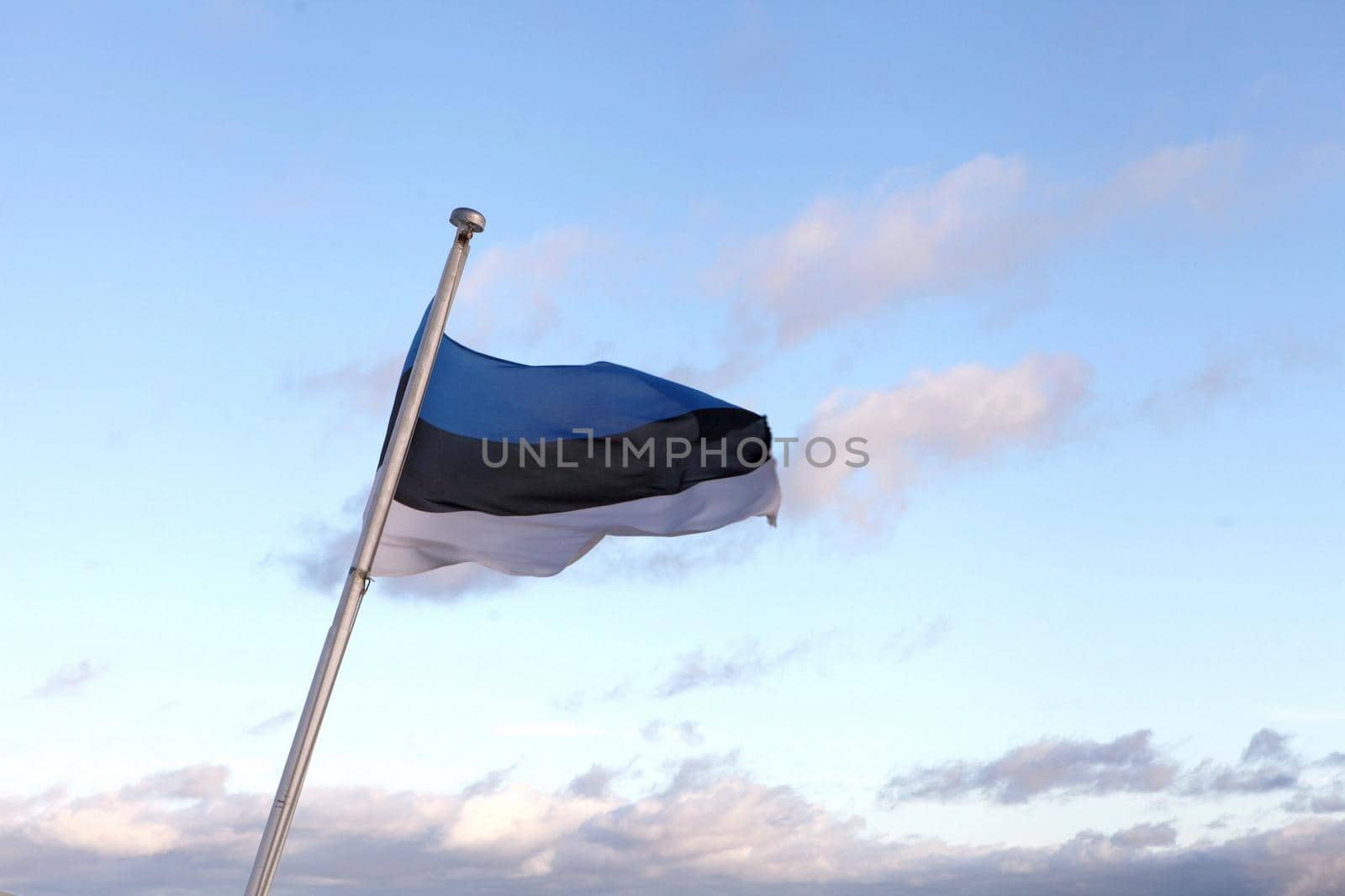 Flag of Estonia flying in the wind. Estonian tricolor behind blue sky