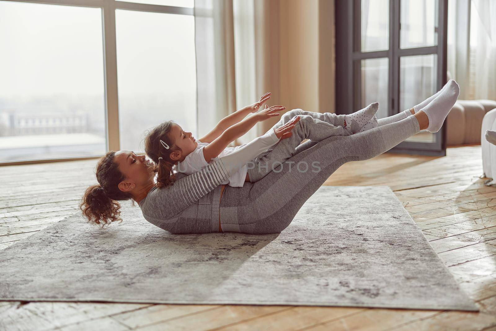 Happy woman exercising with daughter at home by Yaroslav_astakhov