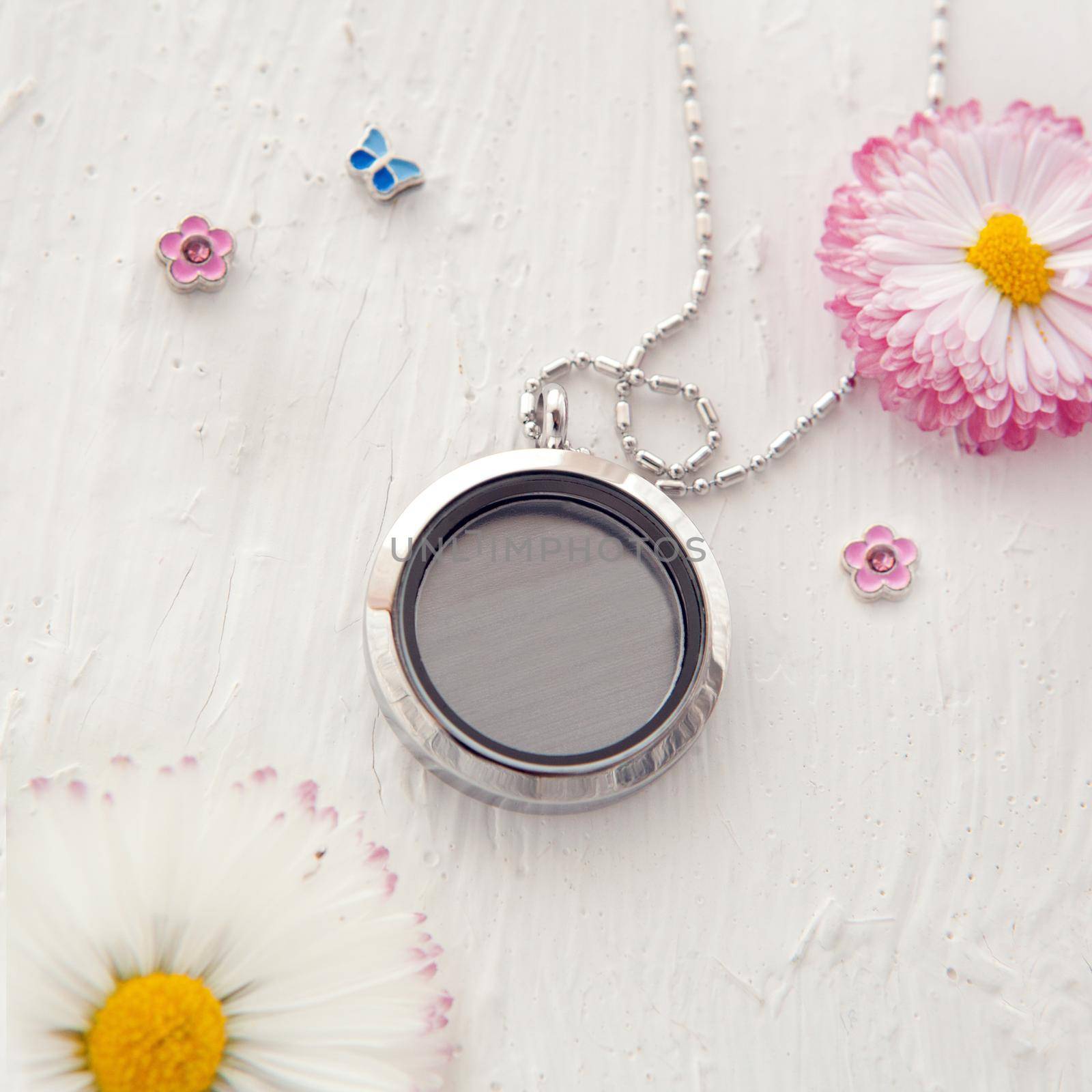 Silver necklace for woman shining on white table with pink daisy flowers. Luxury silver jewelry chains with glass. Small Beautiful precious metal present for woman. Bellis perennis and expressions