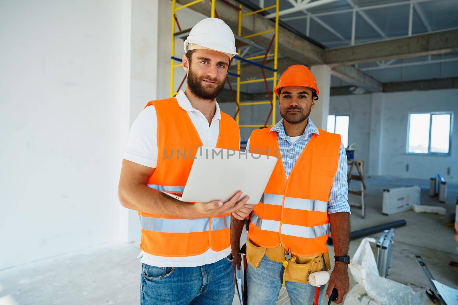 Two specialists supervisors in hardhats using laptop at construction site for work, close up