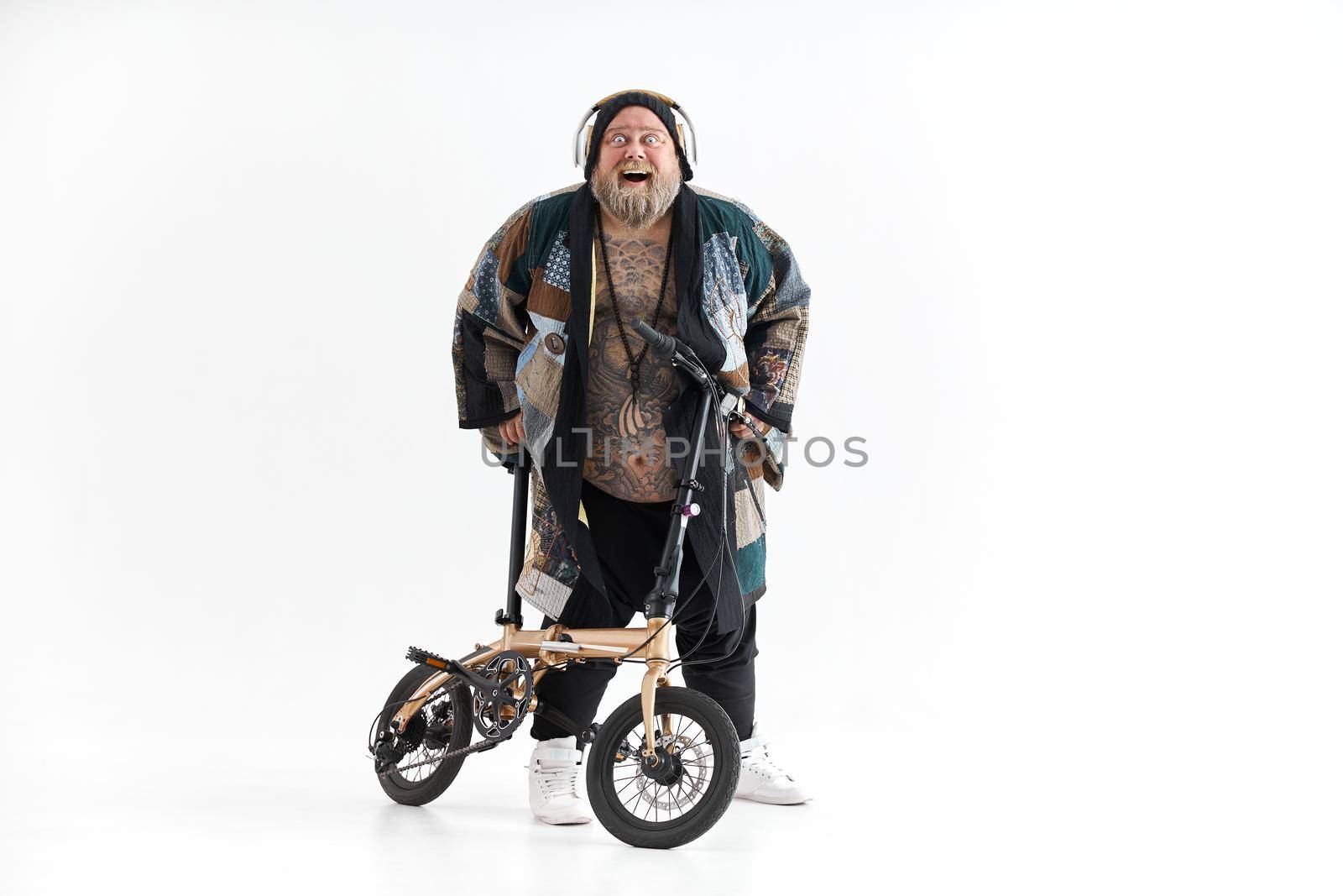 Big fat tattoed caucasian man in kimono is holding little bicycle and smilling