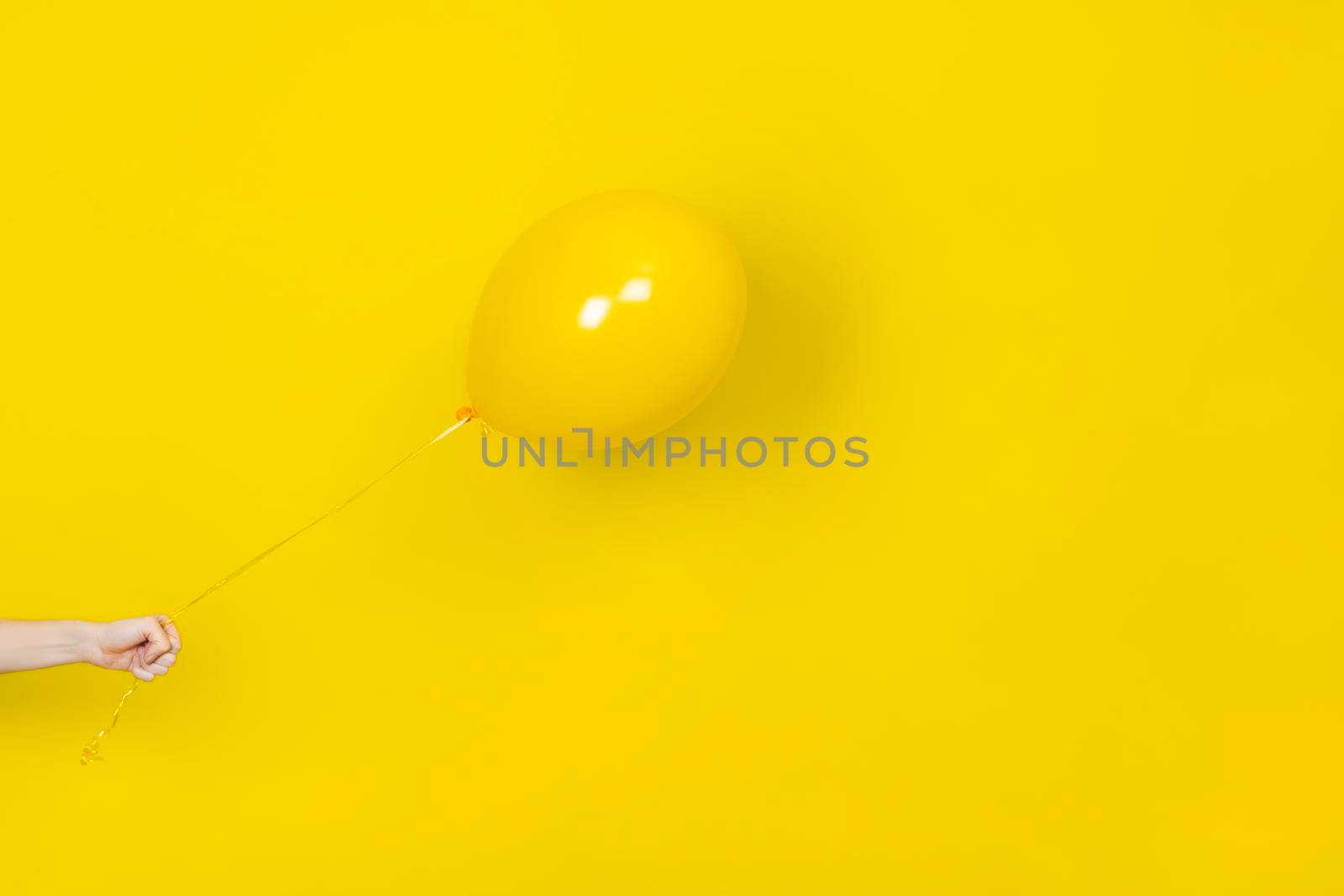 Female hand hold flying yellow balloon. Party or present concept. Yellow Balloon and hand isolated on yellow backgroun. Monochrome banner with copy space