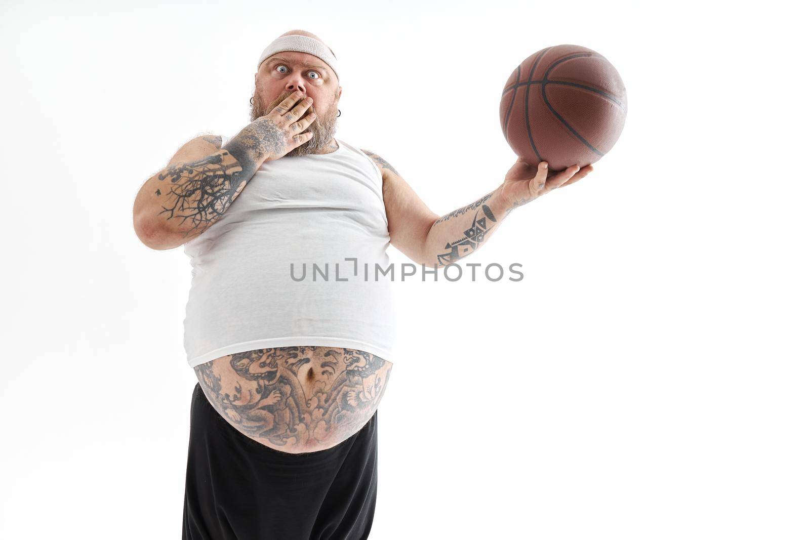 bearded fat caucasian tattoed man with basketball ball in white background. He is funny and happy