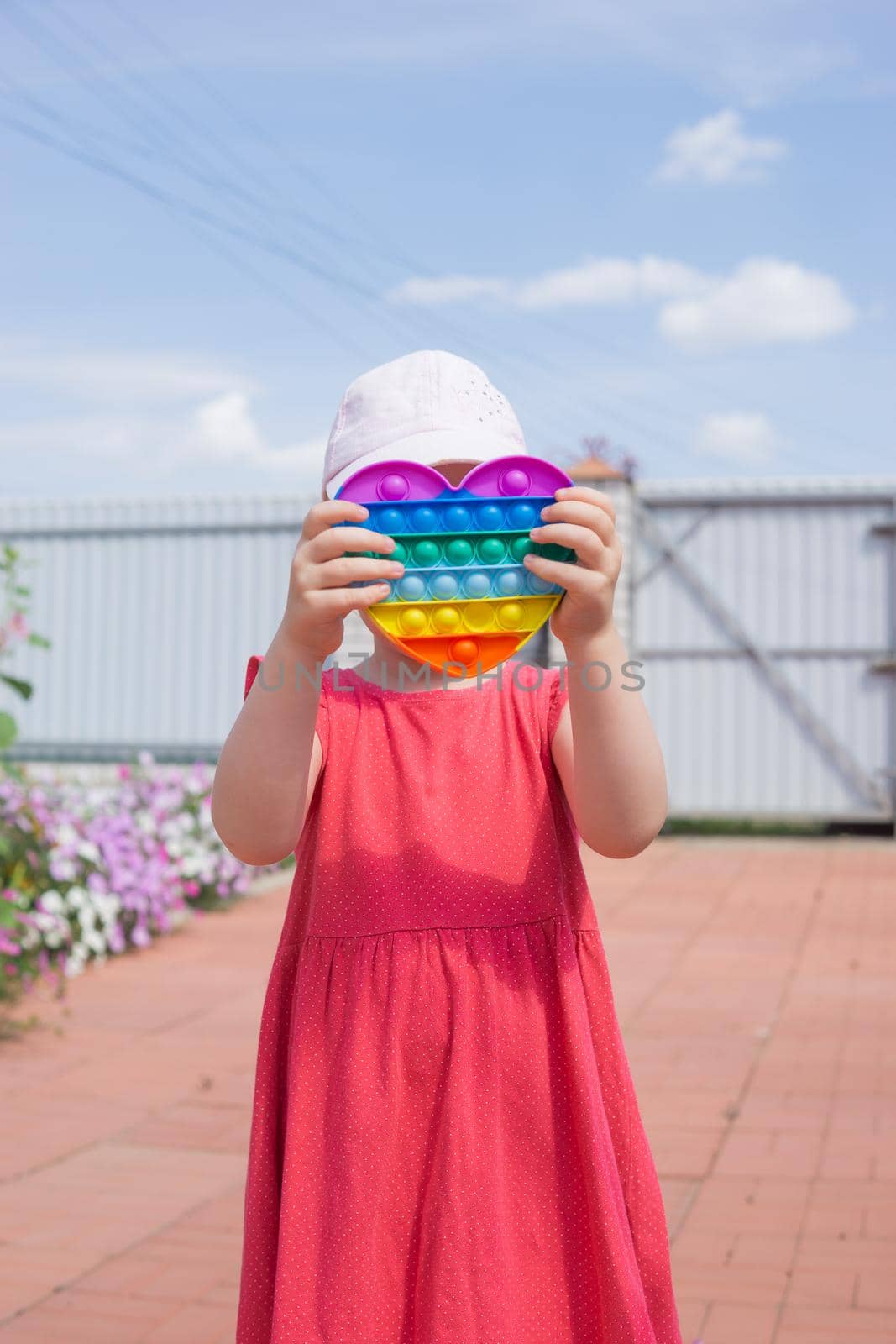 Cute caucasian fair hair girl in pink dress is playing and showing funny trendy silicone antistress colorful toy popit. Push Popper fidget toy is the ideal toy to get rid of your frustration or stress.