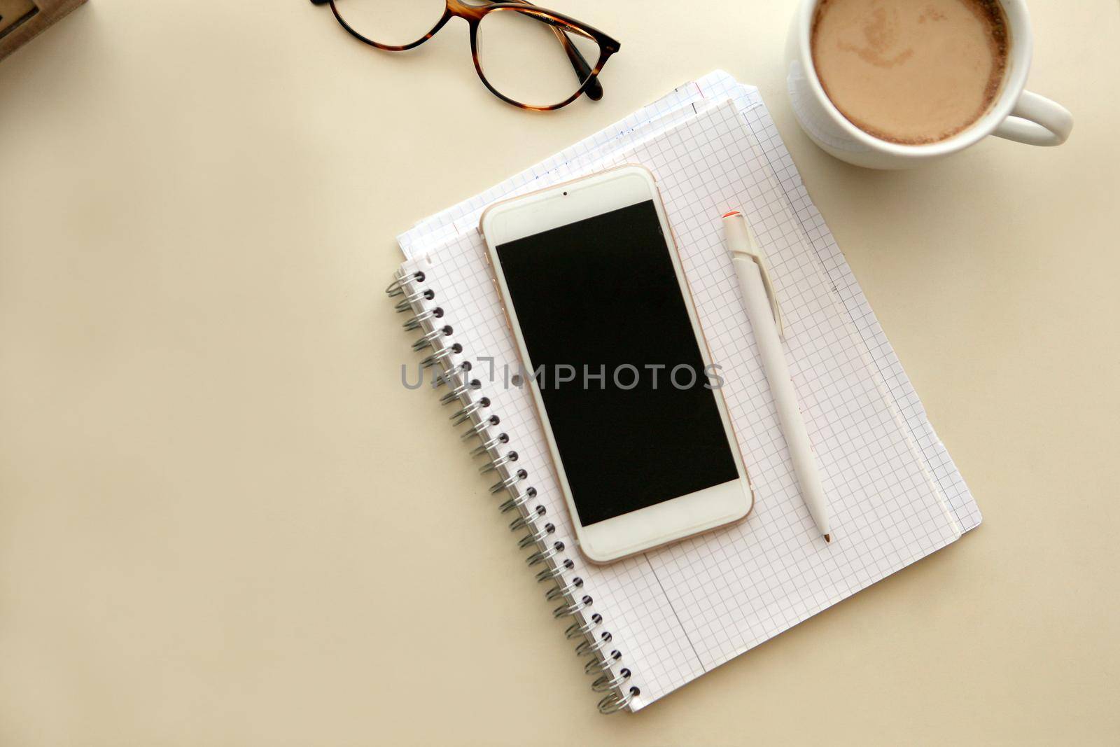 Mobile phone and notes paper. Retro style interior - cozy working place at home stylish interior in warm pastel colors, table and white coffee mug with glasses. stay at home - a place for home office or a place to relax.