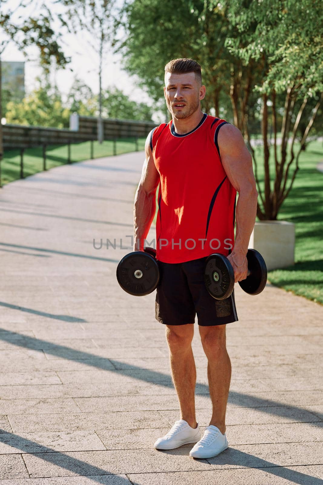 athletic man with dumbbells in his hands outdoors in the park by Vichizh