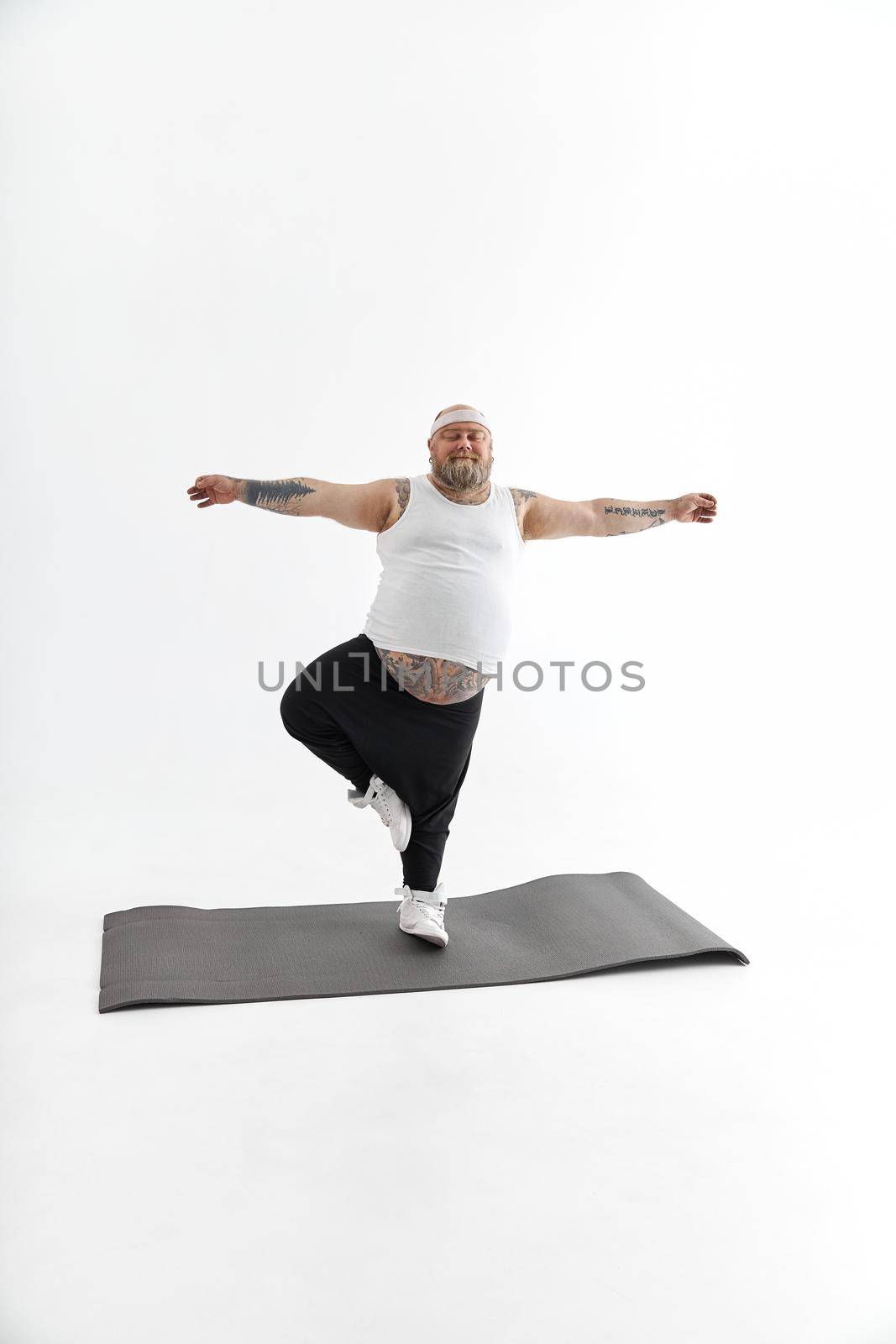 Sporty fat man with beard and tattoos is doing yoga