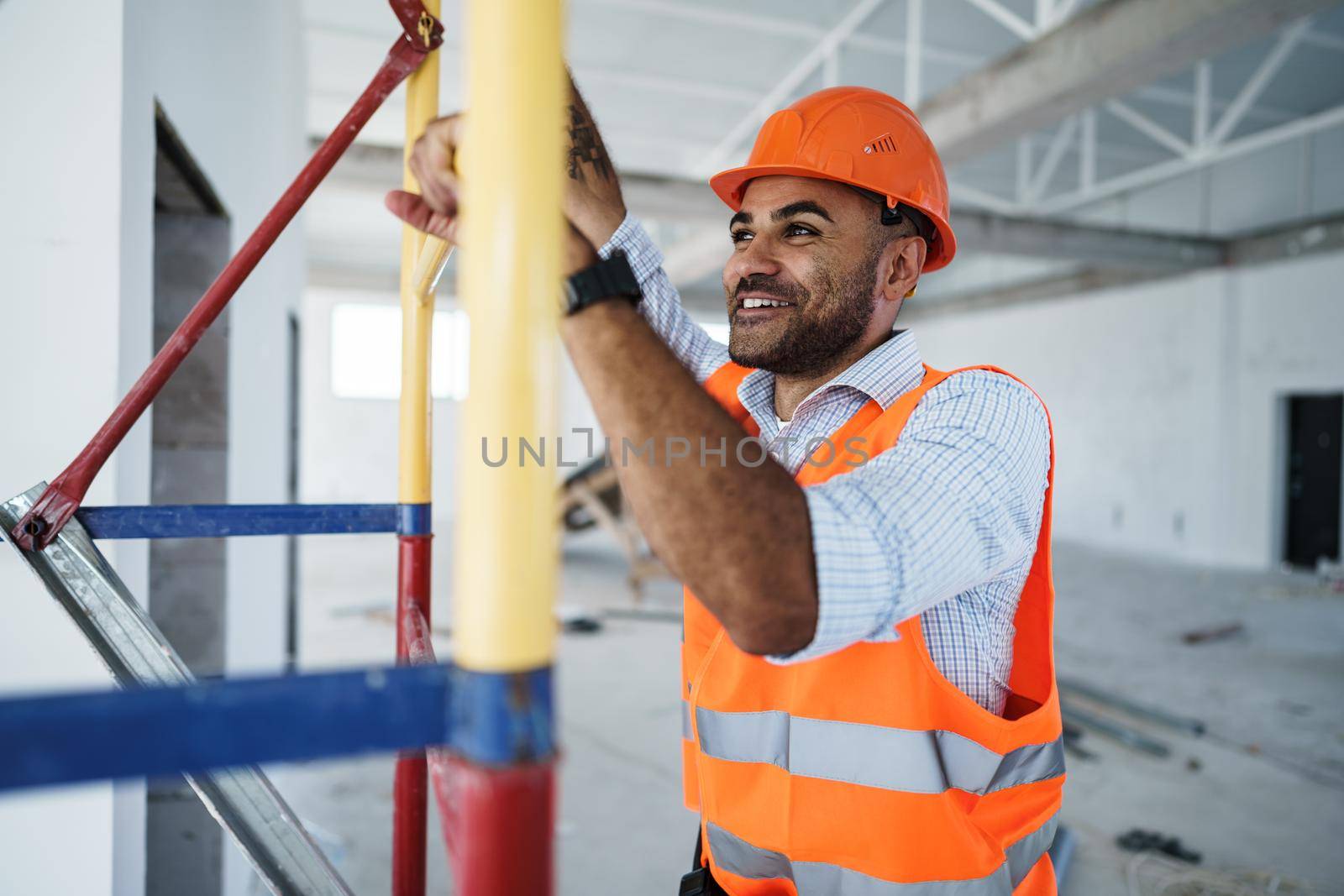 Young handsome builder climbing on scaffolding at construction site, close up