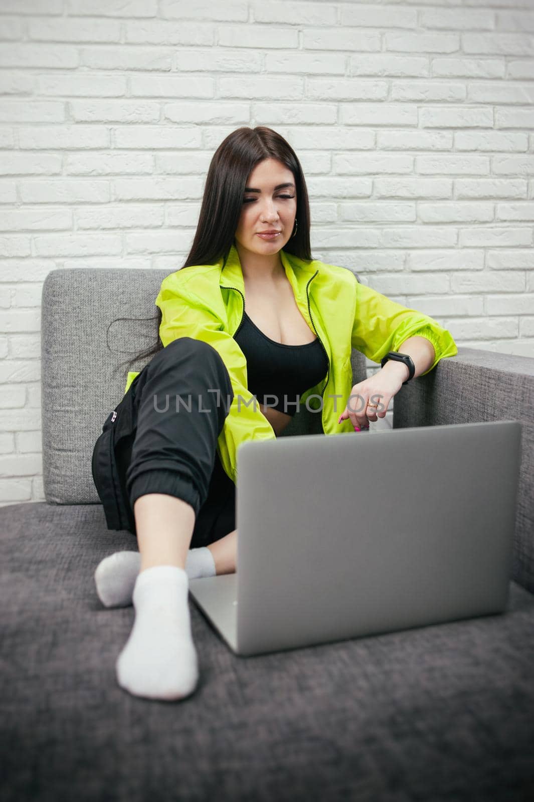 girl in a bright tracksuit with a laptop on the couch
