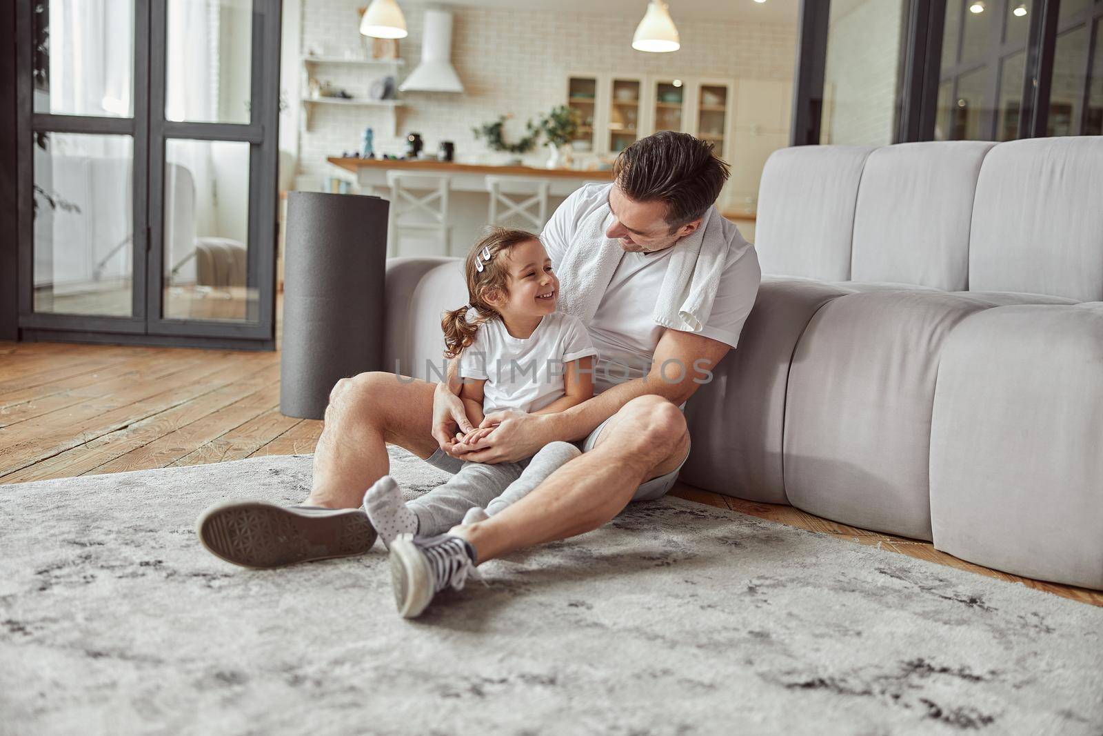 Cheerful little girl is sitting on floor with dad and cuddling while staying together at home