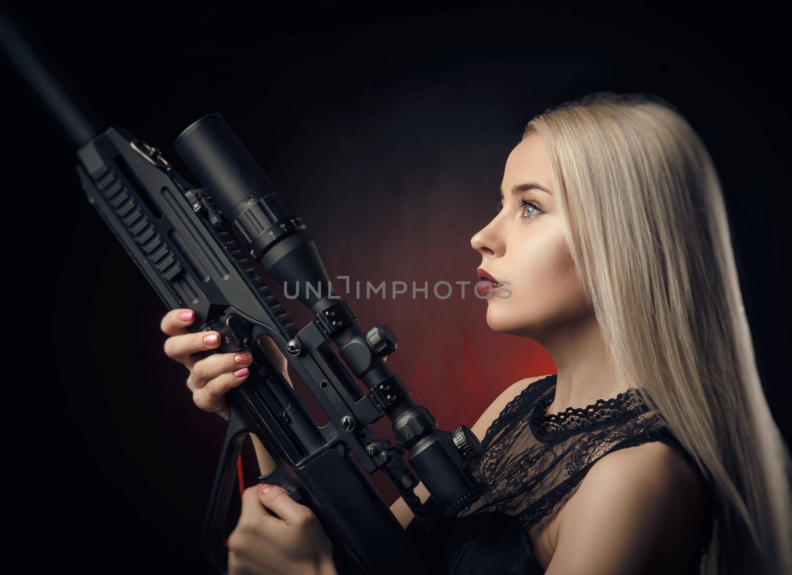 the young blonde girl in black dress posing on black background with weapon