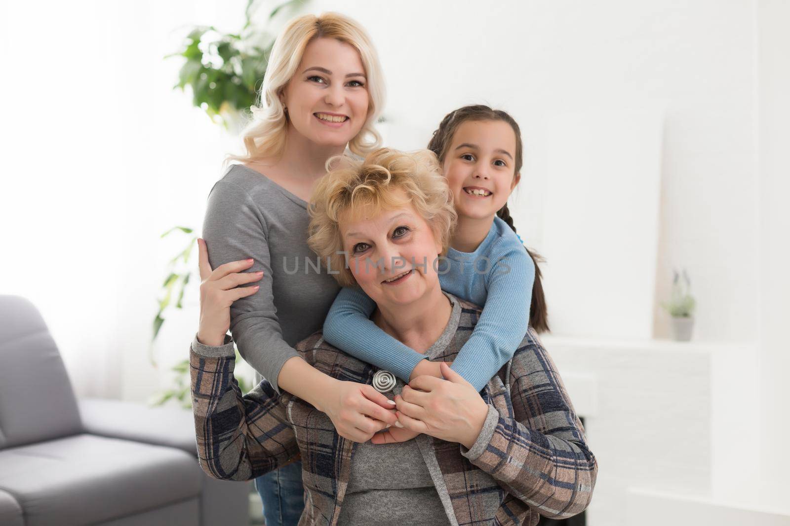 Three generations of women. Beautiful woman and teenage girl are kissing their granny while sitting on couch at home by Andelov13
