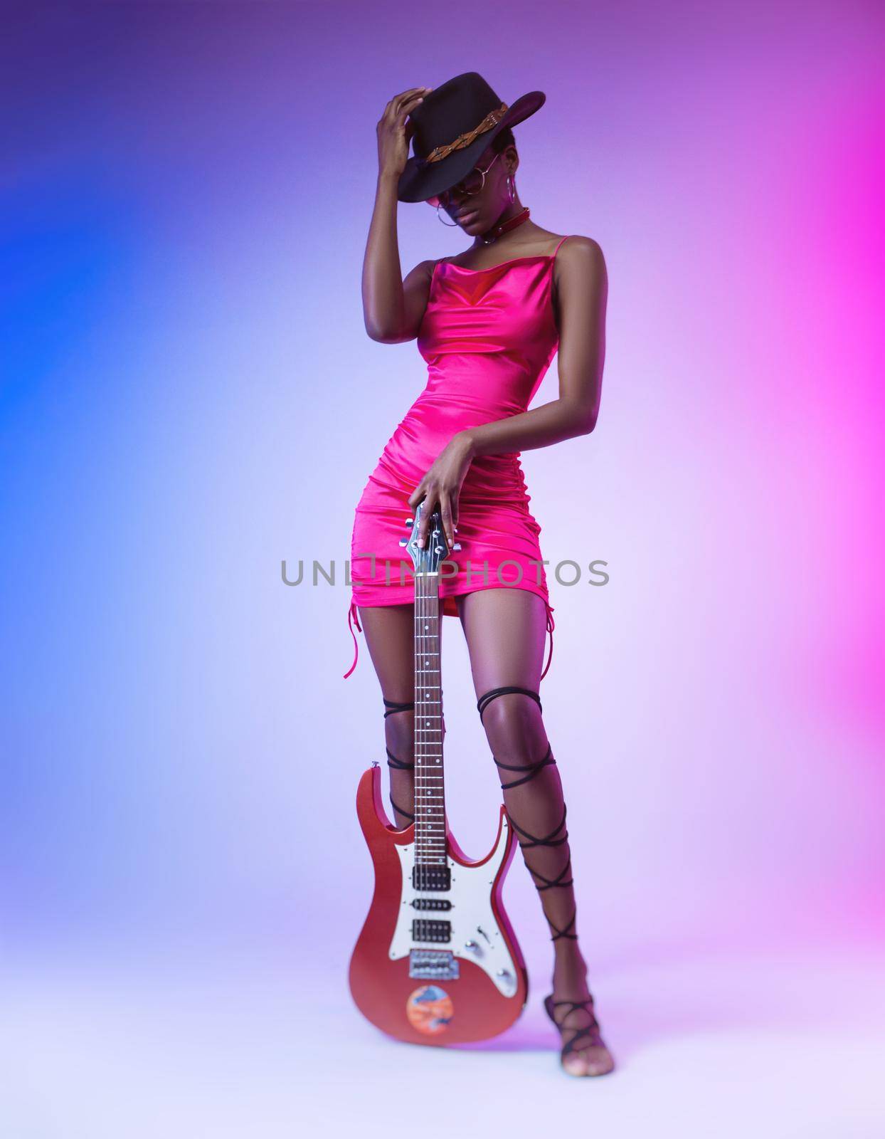 the dark-skinned woman in a pink short dress and a hat with an electric guitar