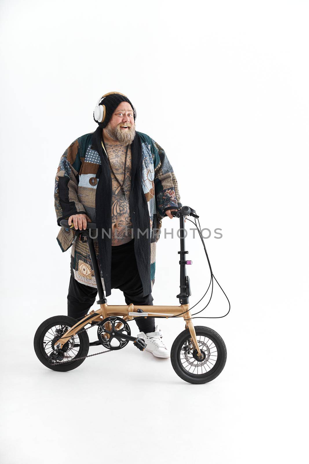 Big fat tattoed caucasian man in kimono is holding little bicycle and smilling