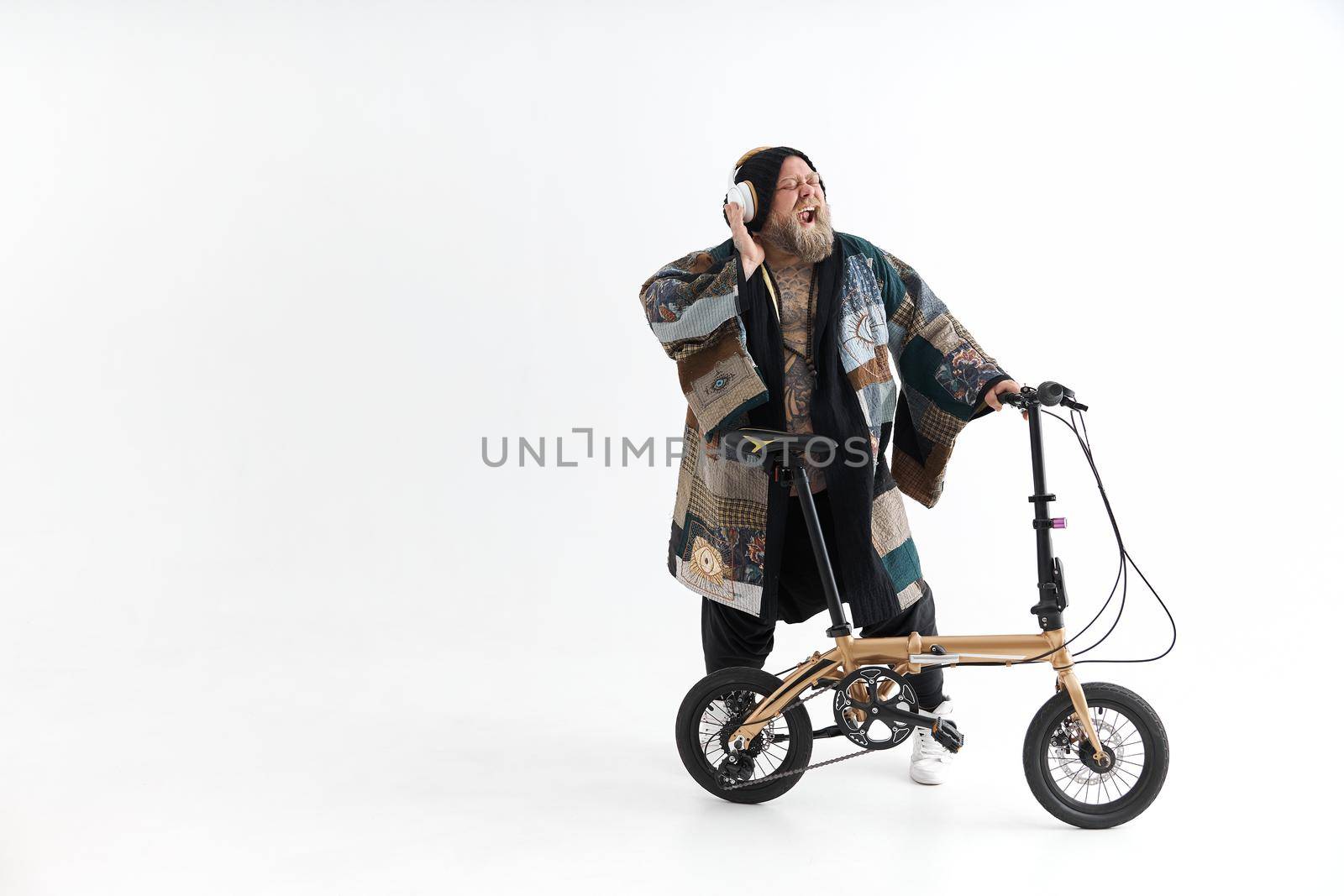 Big fat tattoed caucasian man in kimono is holding little bicycle and smilling by Yaroslav_astakhov