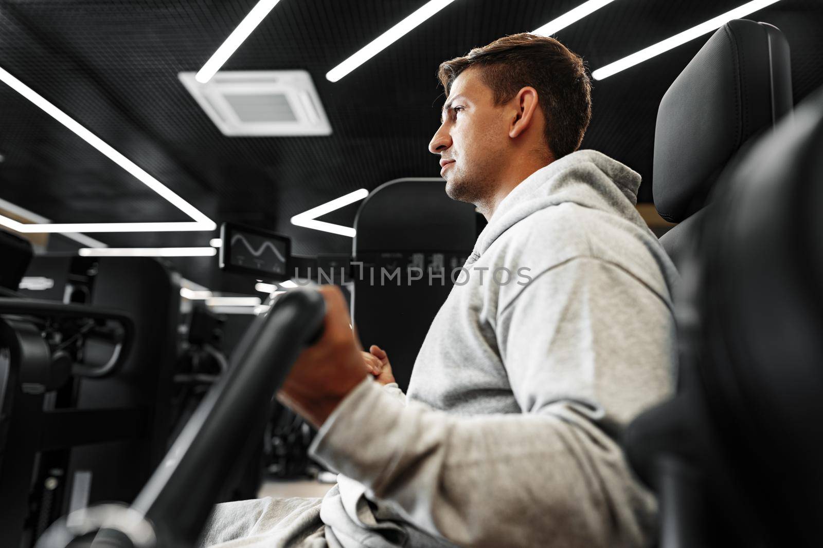 Young fit bodybuilder man doing arms workout training in the gym on machine, close up