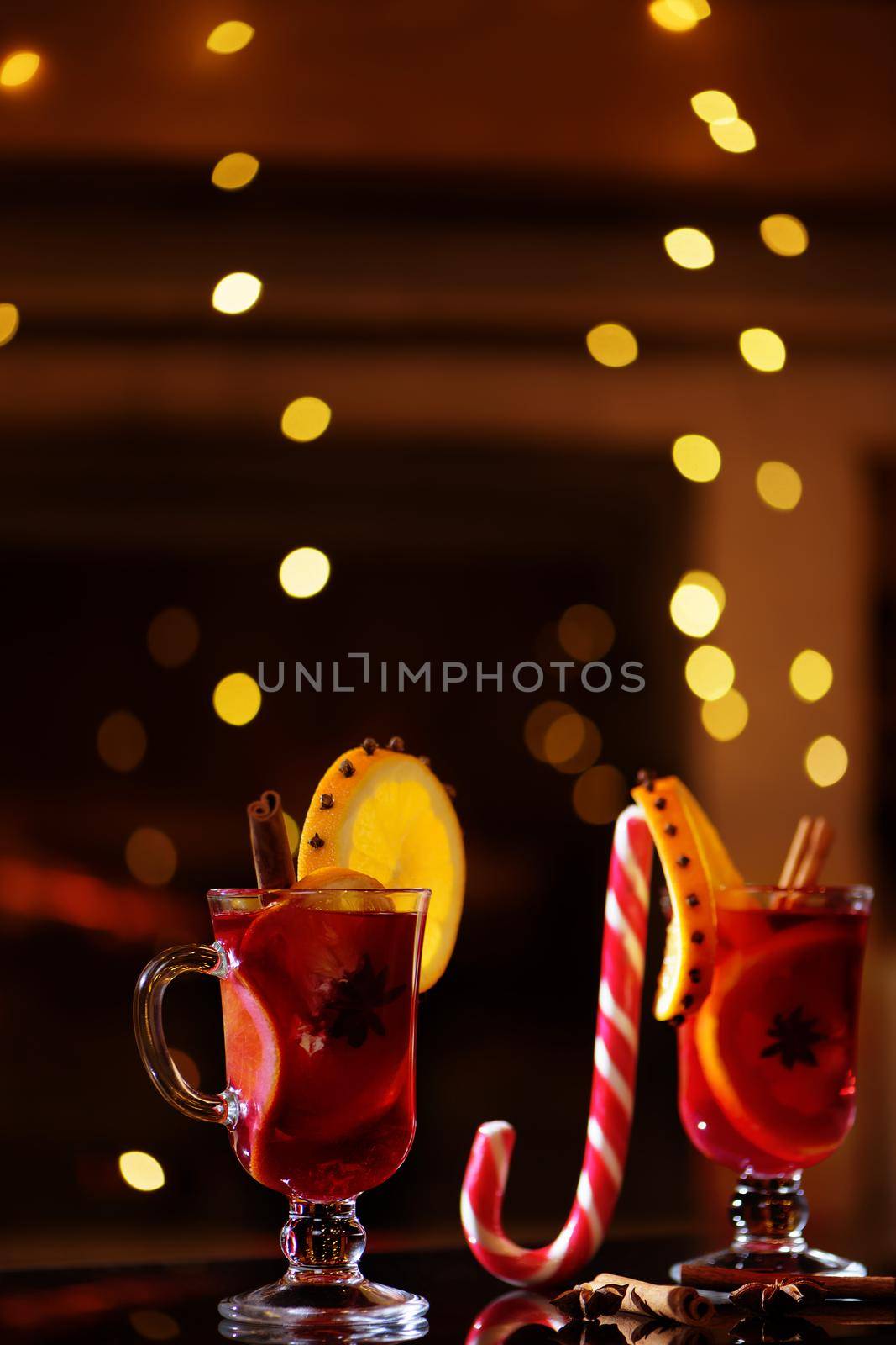 Delicious winter mulled wine with oranges at romantic fireplace with falling stars on background.