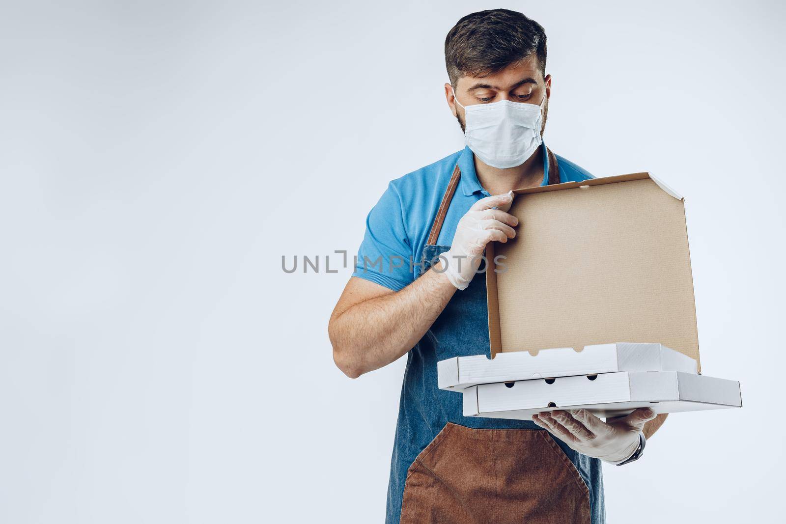 Pizza delivery man in medical gloves and mask against grey background. Safe service while coronavirus covid-19 outbreak