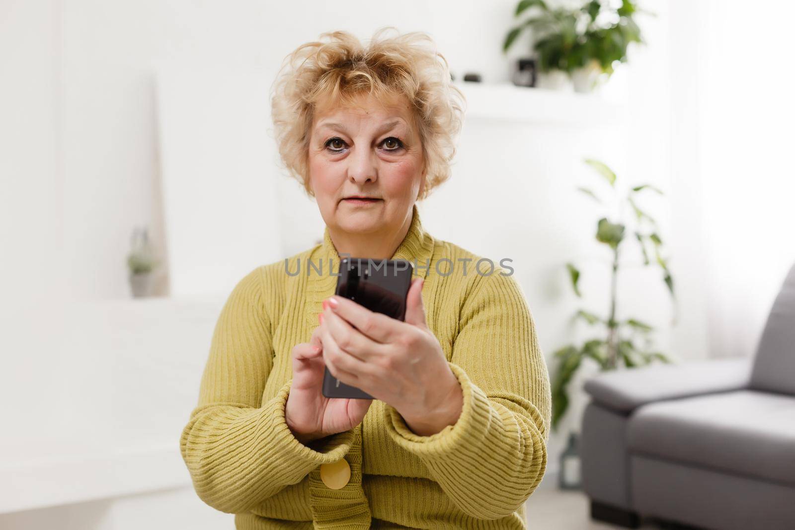 Concept of easy, fast usage of modern technology among all ages. Portrait of confident mature woman with wrinkles she is using her modern smartphone for sending a message isolated on gray background