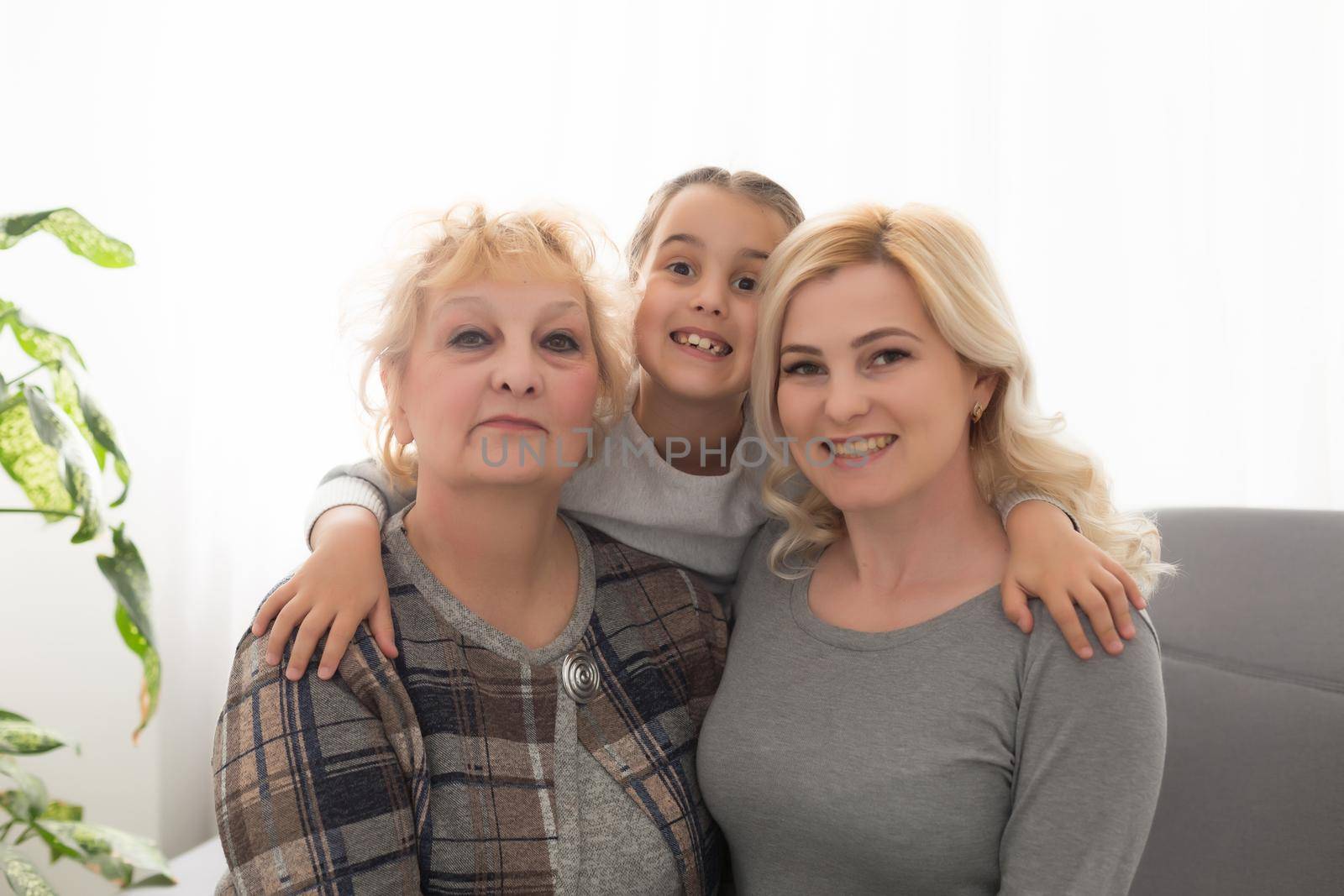 Three generations of women. Beautiful woman and teenage girl are kissing their granny while sitting on couch at home