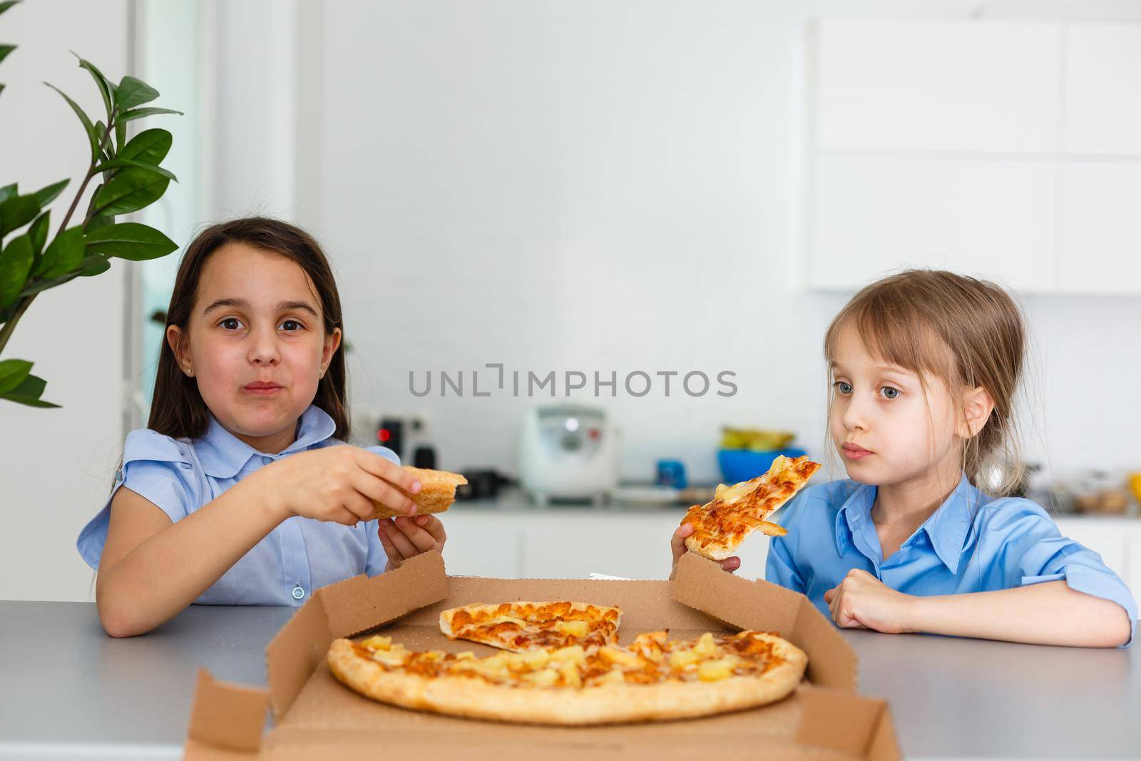 Two happy little child girl friends eating pizza slices.