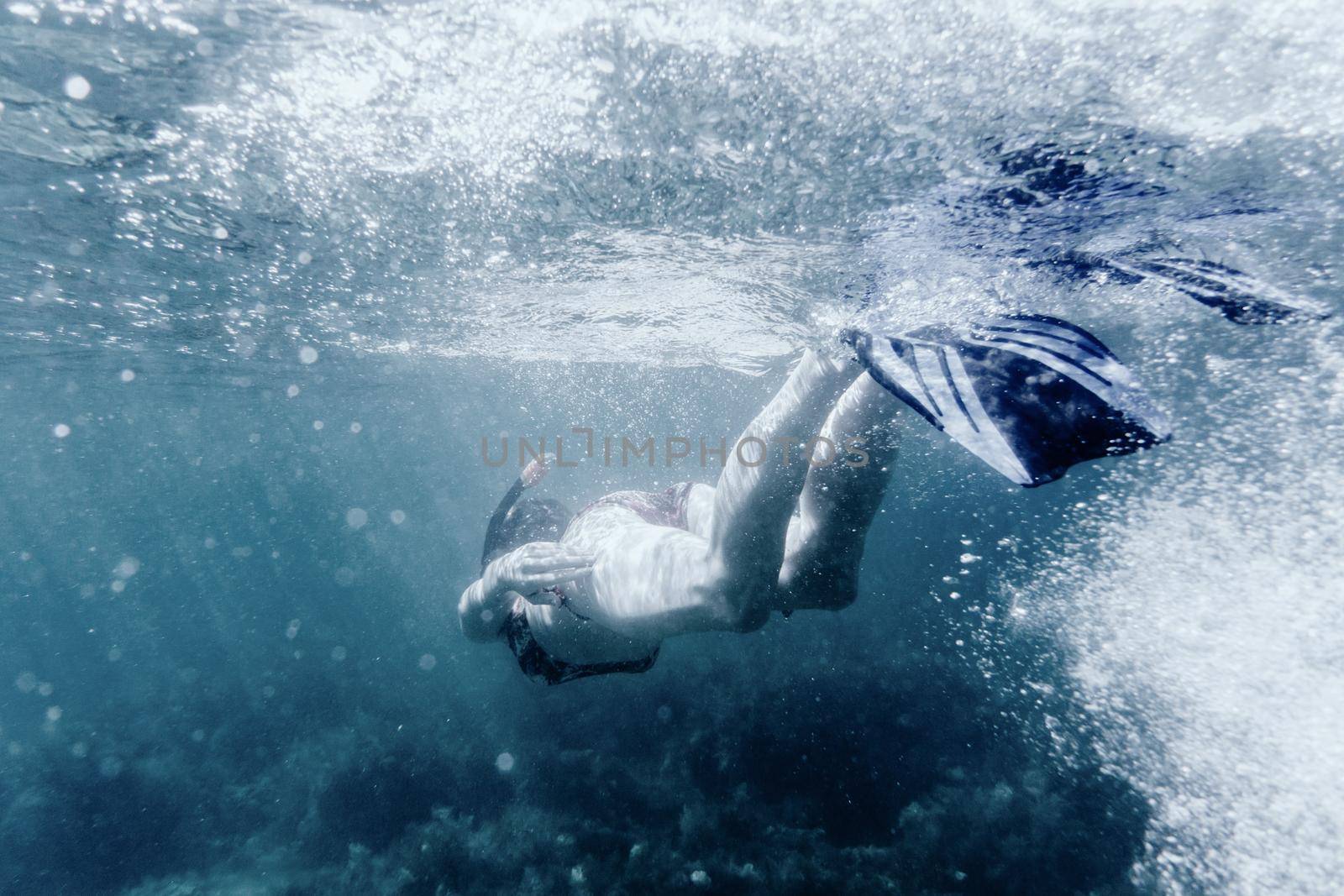 Active young woman freediver in flippers snorkeling underwater, rear view.