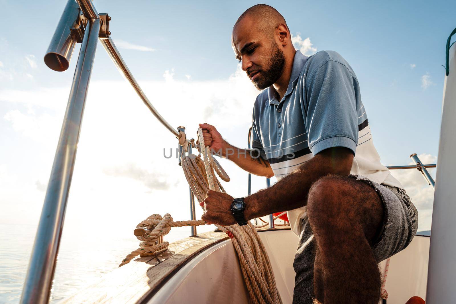 Young african american sailor tying ropes on sailboat in the sea on sunset, close up