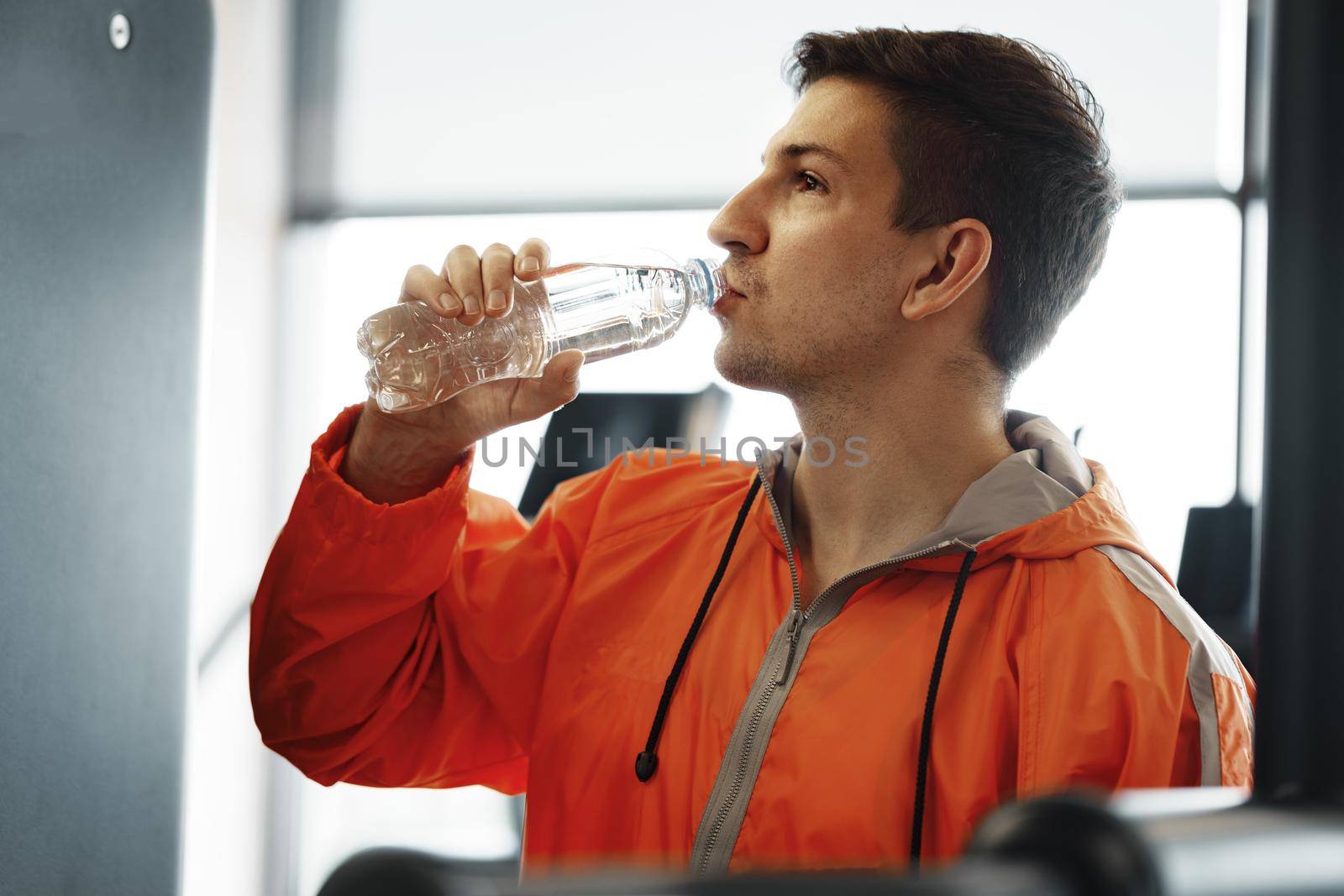 Portrait of young man drinking some water from a bottle in a gym, close up