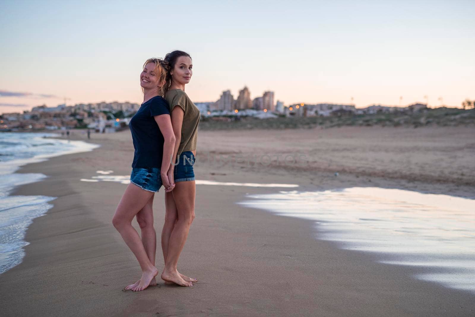 Two pretty young girls pretty best friend women having fun on their summer vacation on Mediterranean sea, mini denim shorts, amazing blonde and brunette hairs, traveling experience, happy emotions by Alexxoma