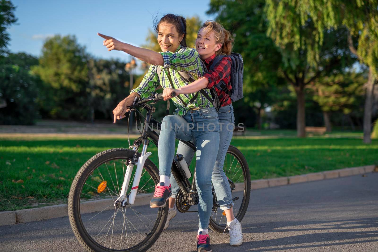 Two pretty young caucasian girls searching the way on a bicycle along the street. Best friends enjoying a day on a bike. Sunny summer evening by Alexxoma