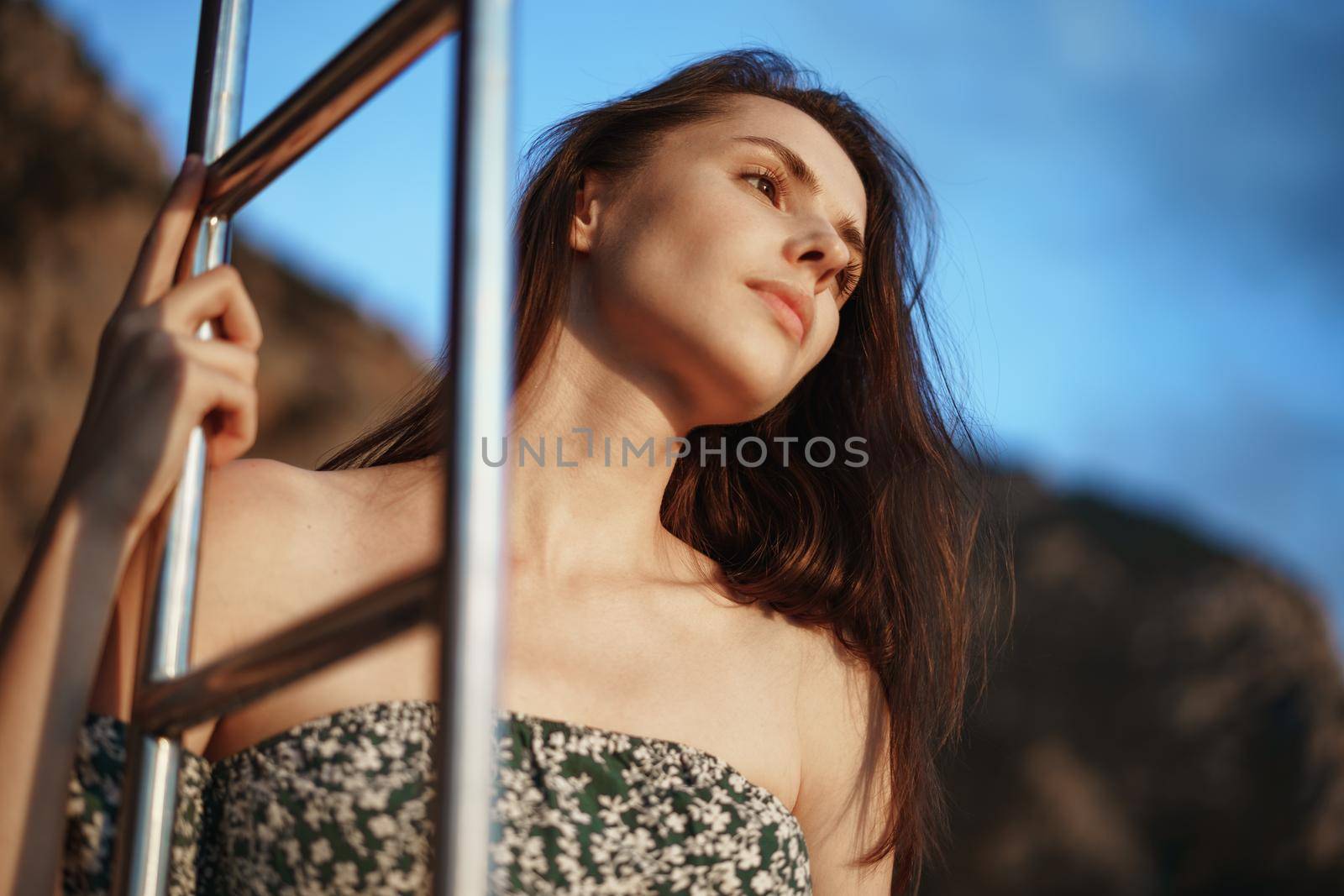 Young pretty woman in floral dress posing on yacht in the sea