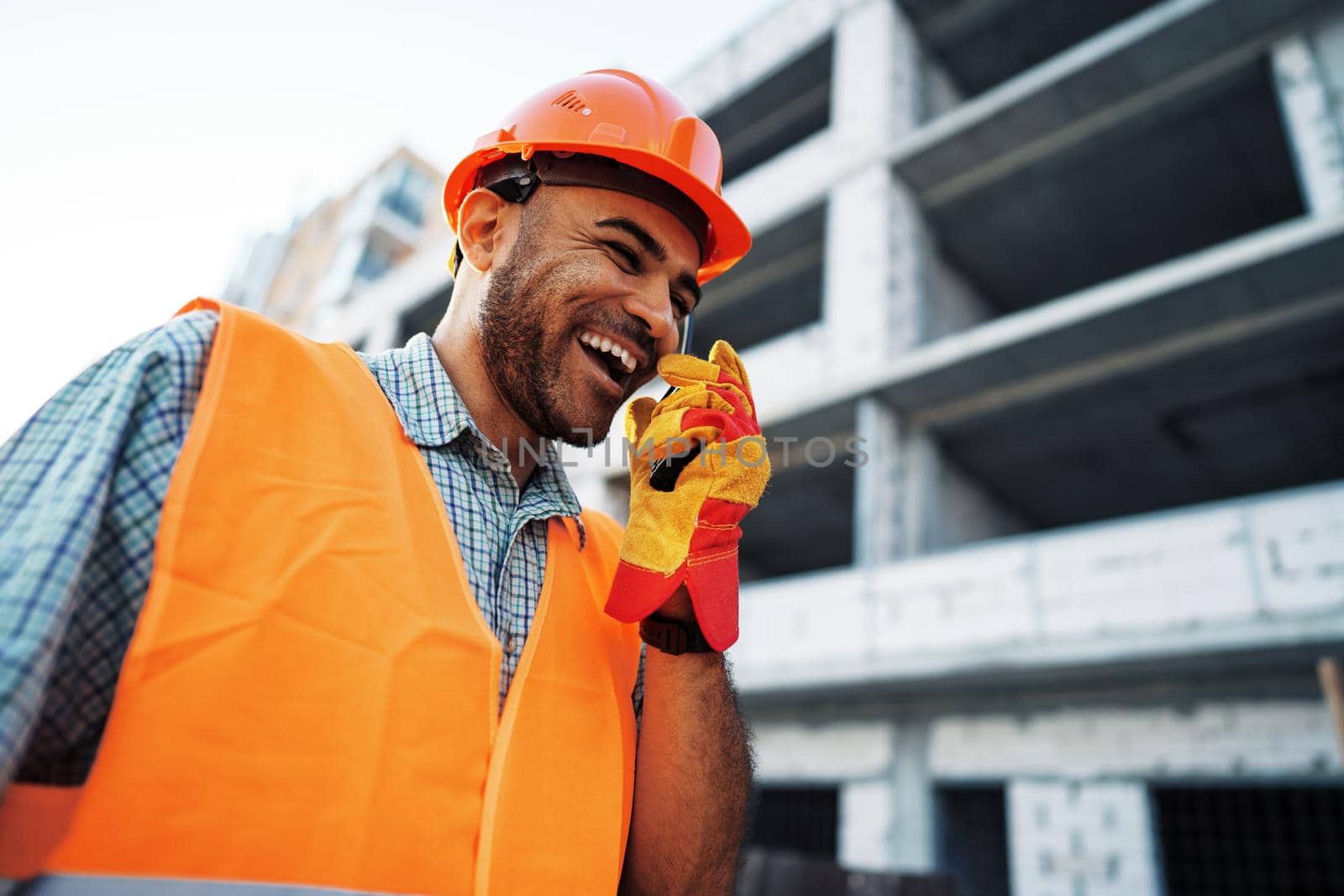 Young construction worker in uniform using walkie talkie on site, close up portrait