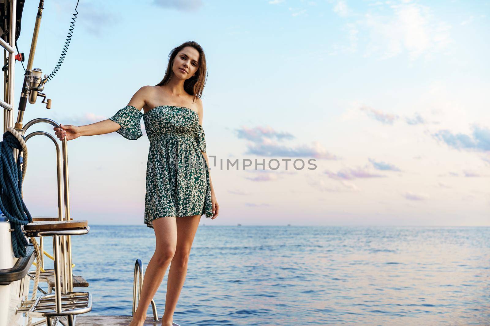 Young pretty woman in floral dress posing on yacht in the sea