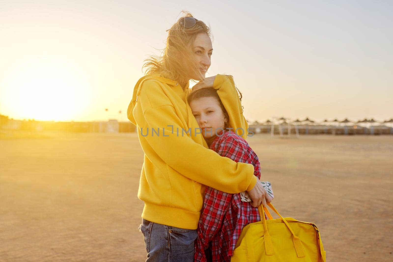 Happy mother and daughter preteen hugging together outdoors, sunset light on beach background. Parent and child, love, relationship, happiness concept