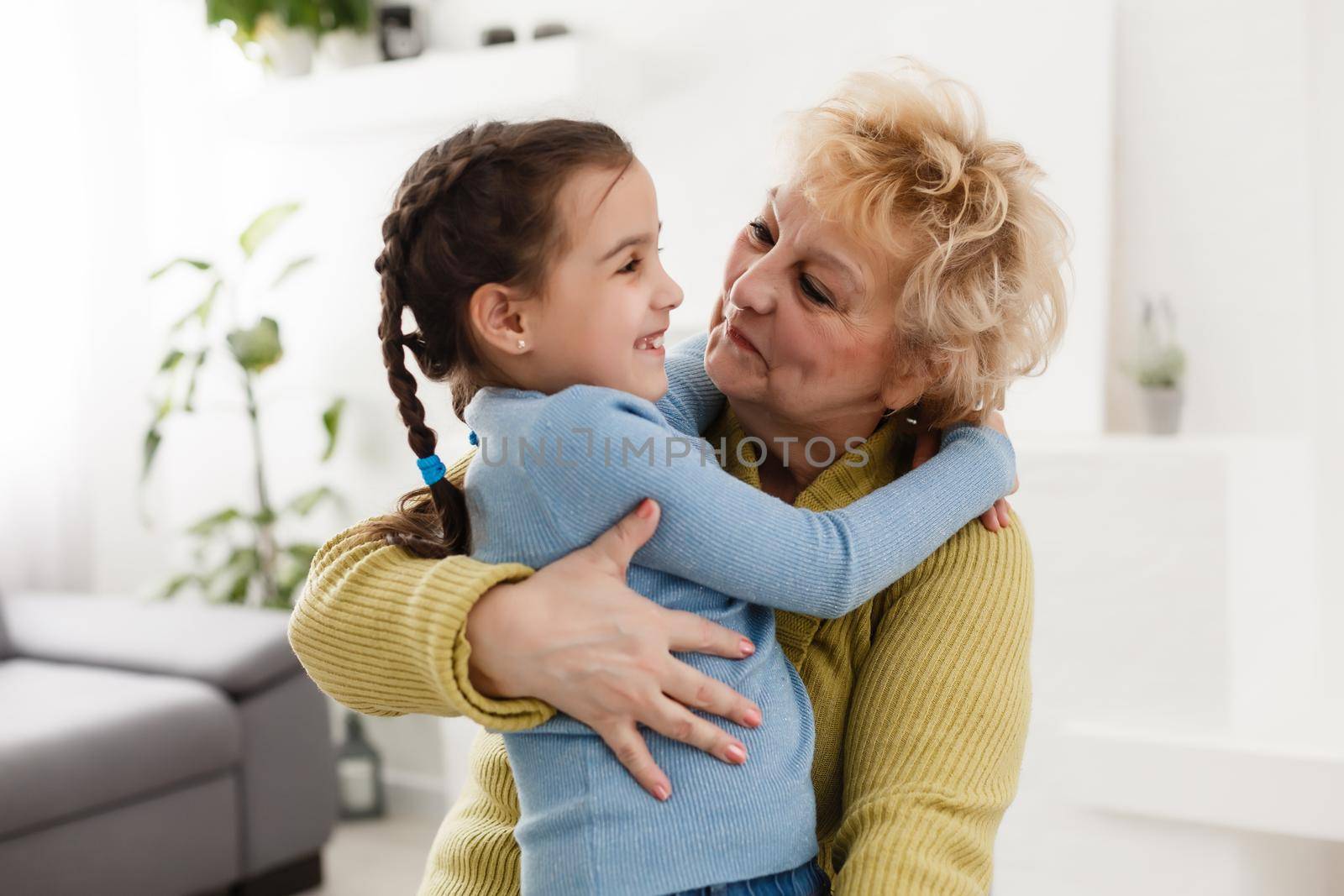 Little granddaughter and happy grandmother giving high five having fun playing together sitting on sofa, smiling grandma granny and preschool grandchild laughing celebrating good relations at home