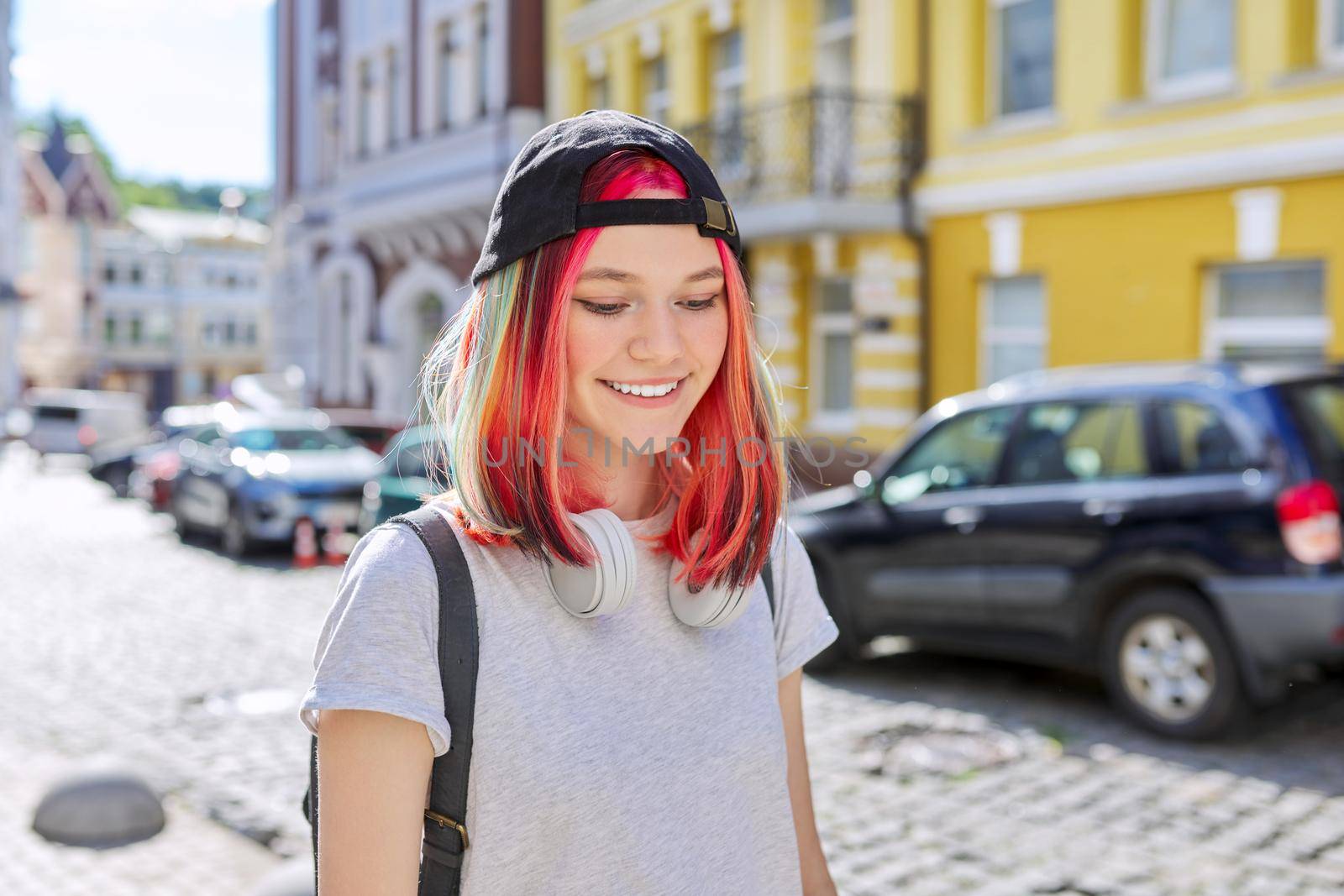 Outdoor urban portrait of a trending female teenager in a cap with a backpack with colored dyed hair. Youth, lifestyle, fashion, urban style, people concept