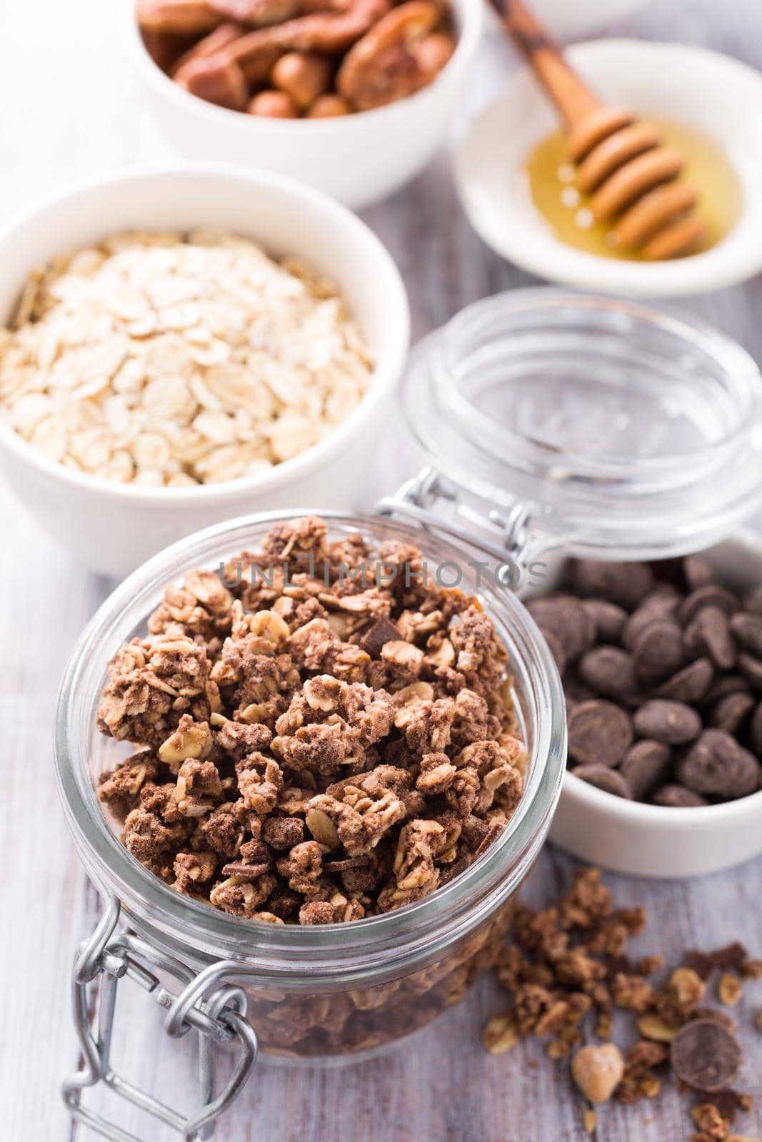 Homemade chocolate granola ingredients, nuts, oats, honey on white wooden background. Healthy breakfast concept.