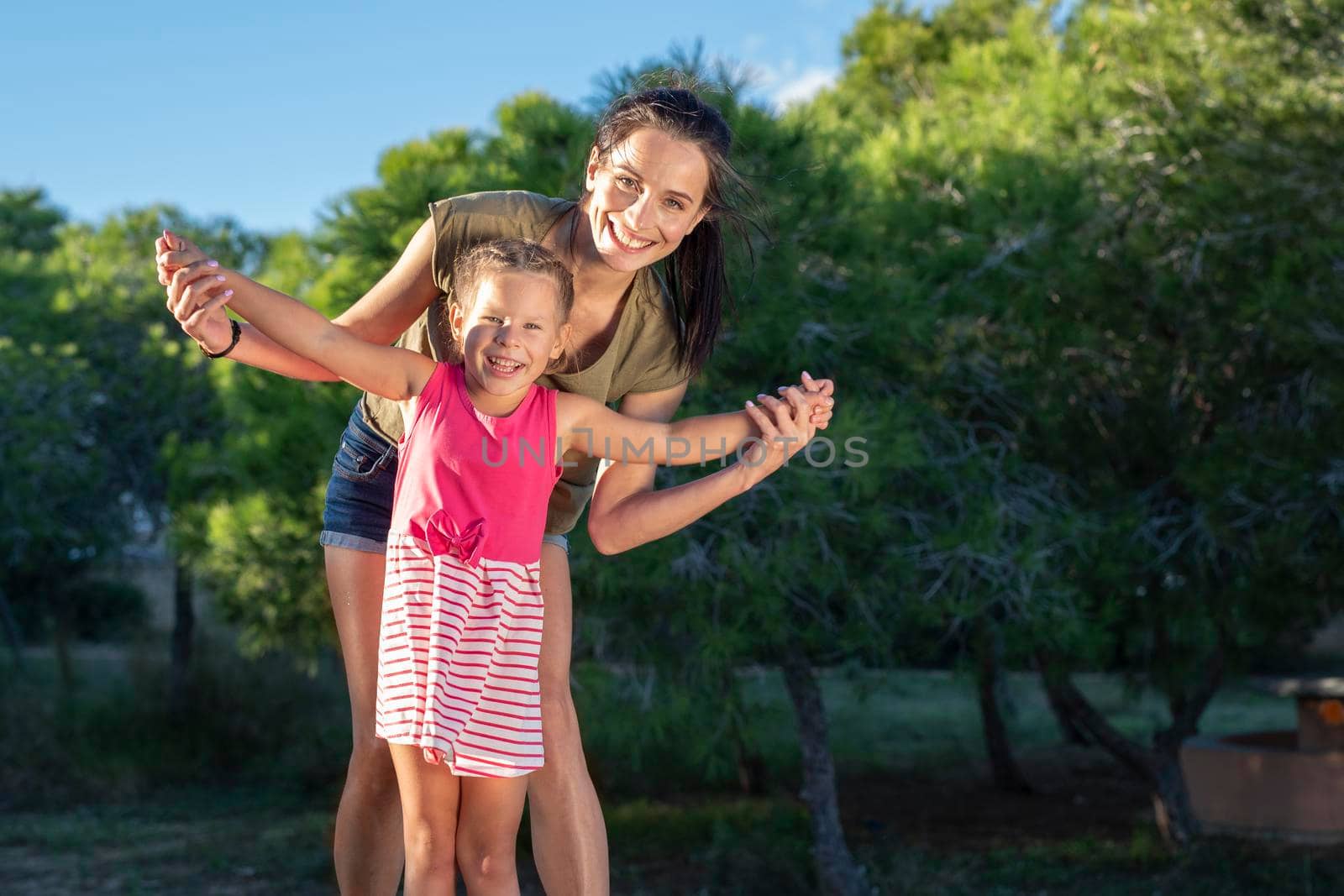 Beautiful mother and her little daughter outdoors. Beauty Mum and her Child playing in Park together at sunset. Outdoor Portrait of happy family. Mother's Day.