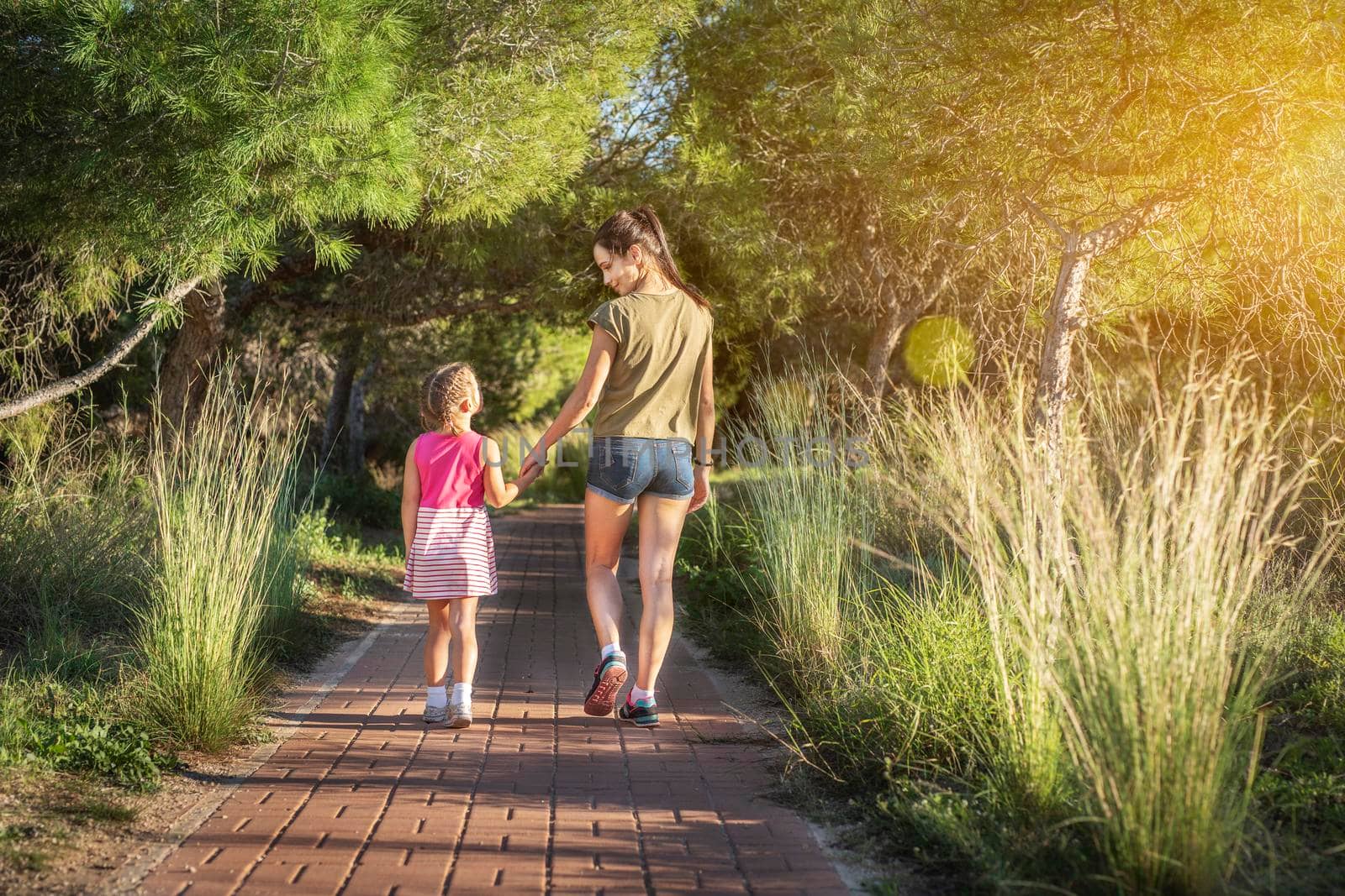 Beautiful mother and her little daughter outdoors. Beauty Mum and her Child walking in Park together at sunset. Outdoor Portrait of happy family. Mother's Day by Alexxoma