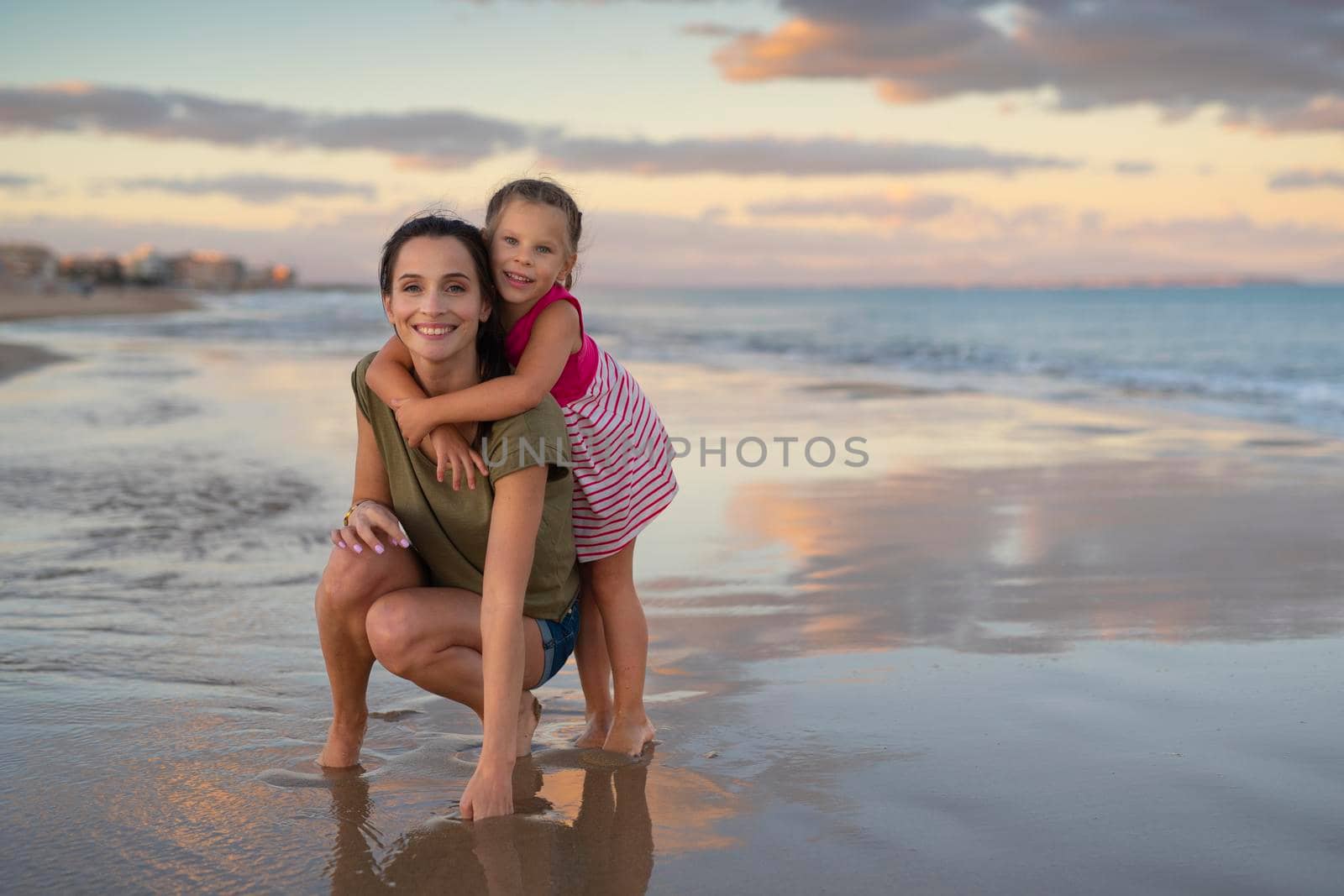 Happy family. Young happy beautiful mother and her daughter having fun on the beach at sunset. Positive human emotions, feelings.