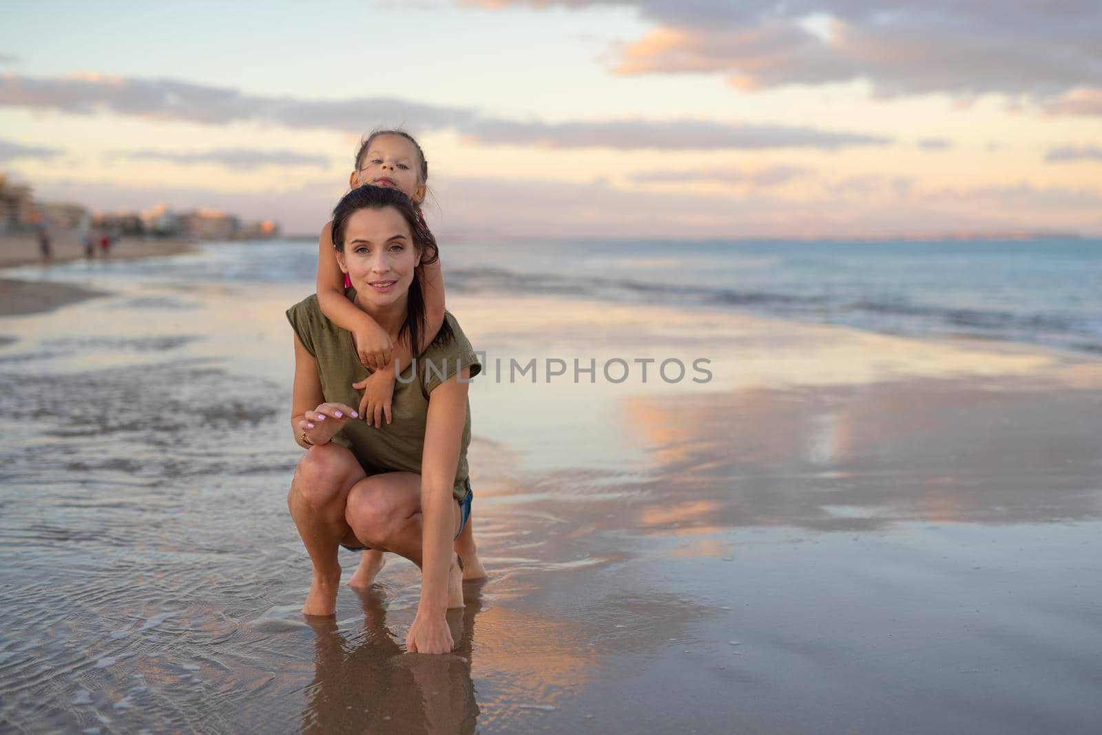 Happy family. Young happy beautiful mother and her daughter having fun on the beach at sunset. Positive human emotions, feelings.