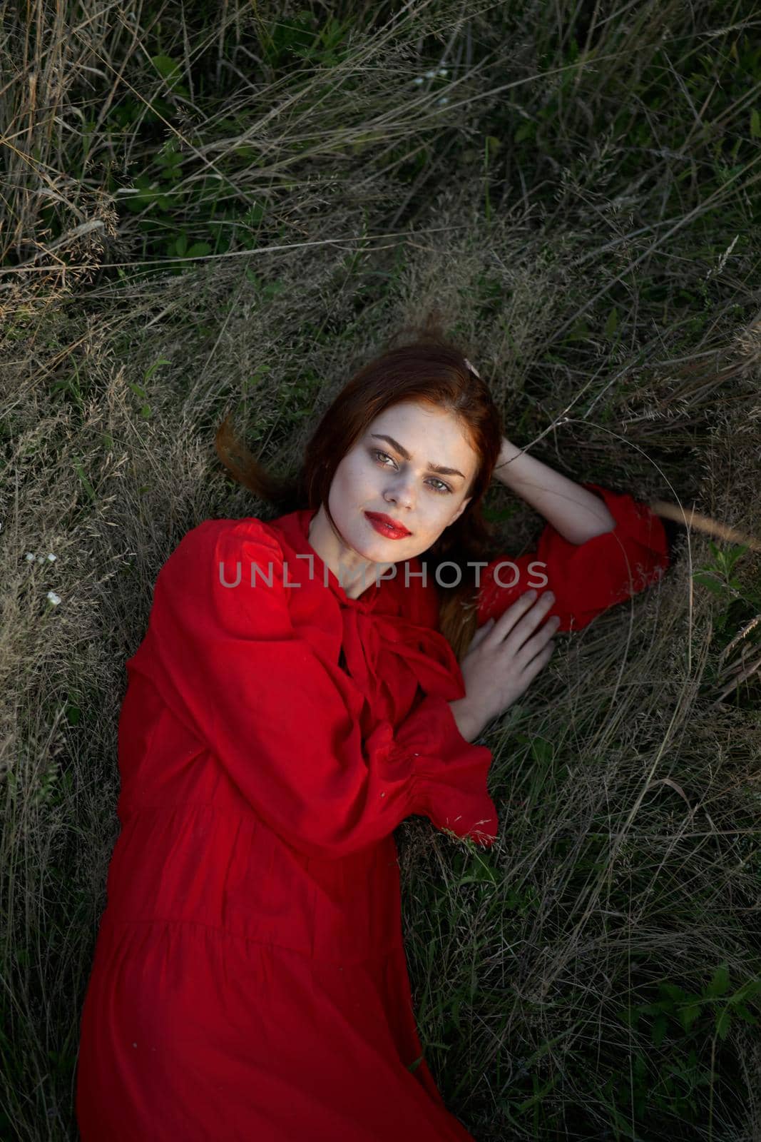 pretty woman in red dress lies on the grass posing top view. High quality photo